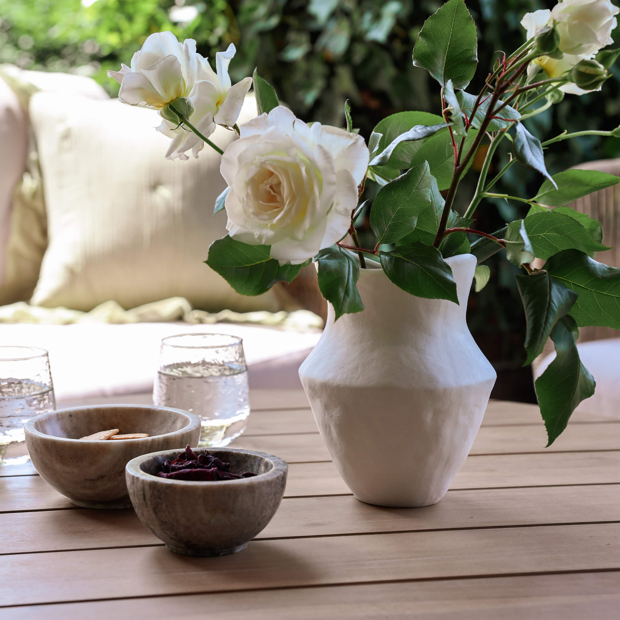 Witte keramische vaas met witte rozen op houten tafel met kommen en glazen water