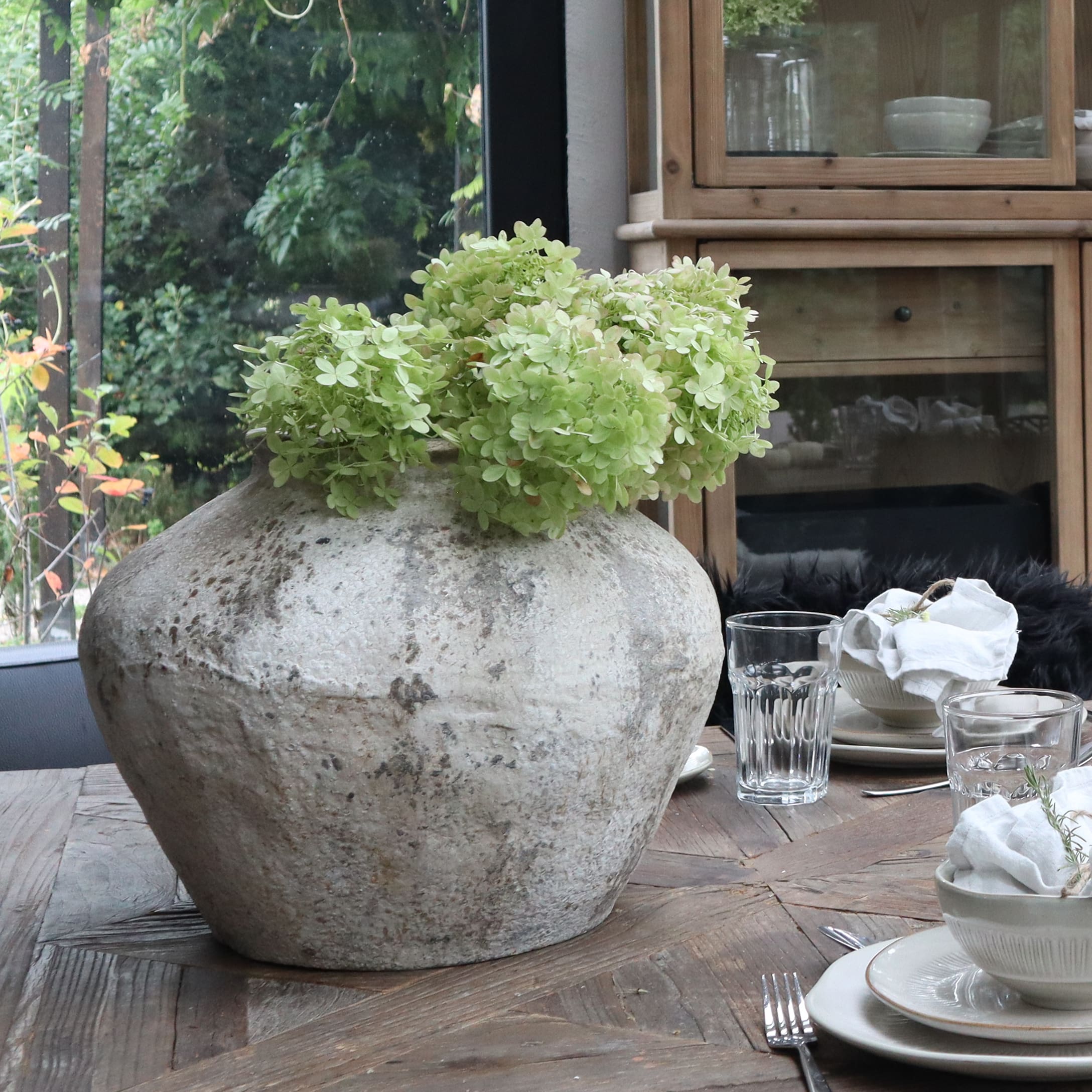 Grote grijze keramische vaas met groene bloemen op houten tafel in eetkamer