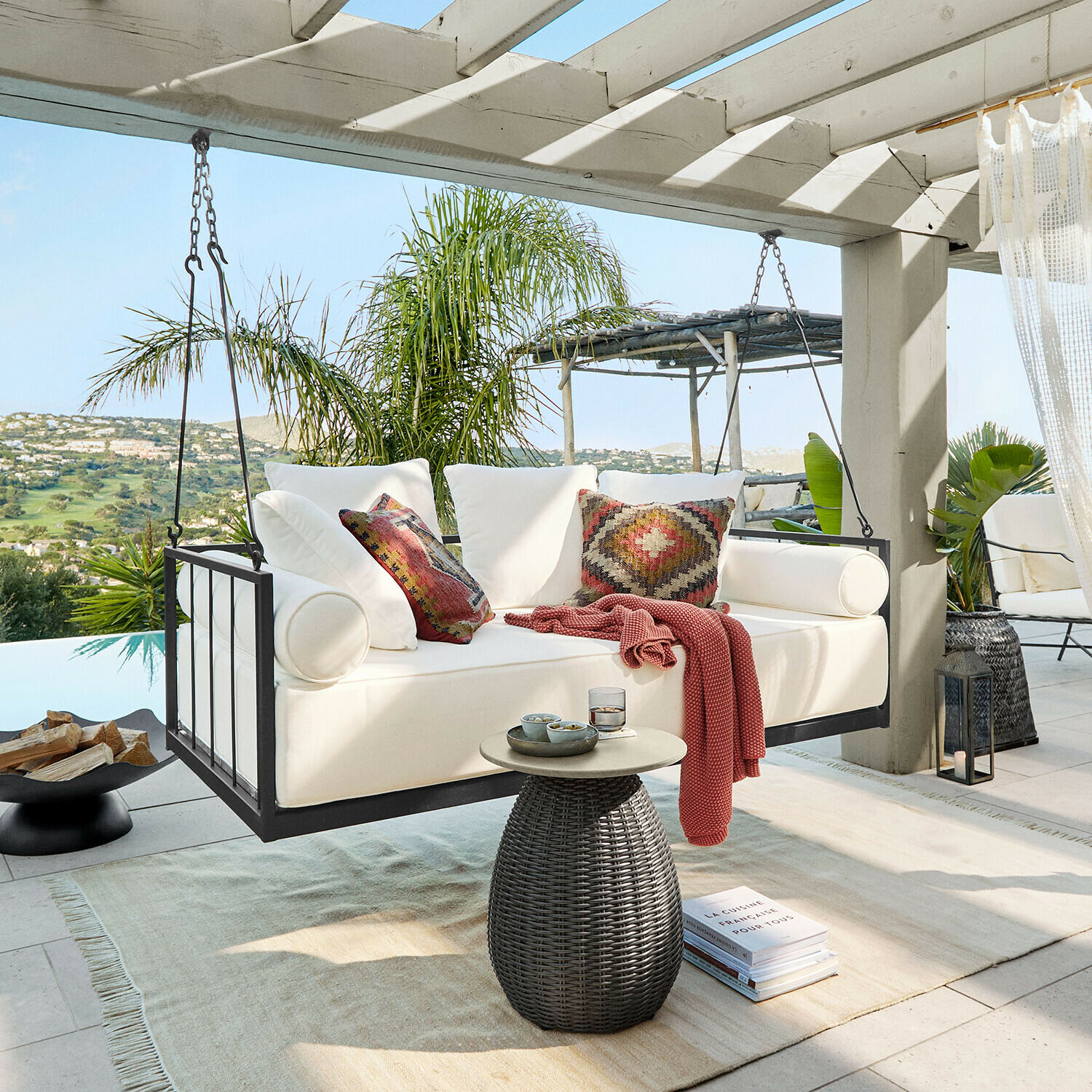 Witte hangbank met metalen frame en kleurrijke kussens op terras met groen uitzicht