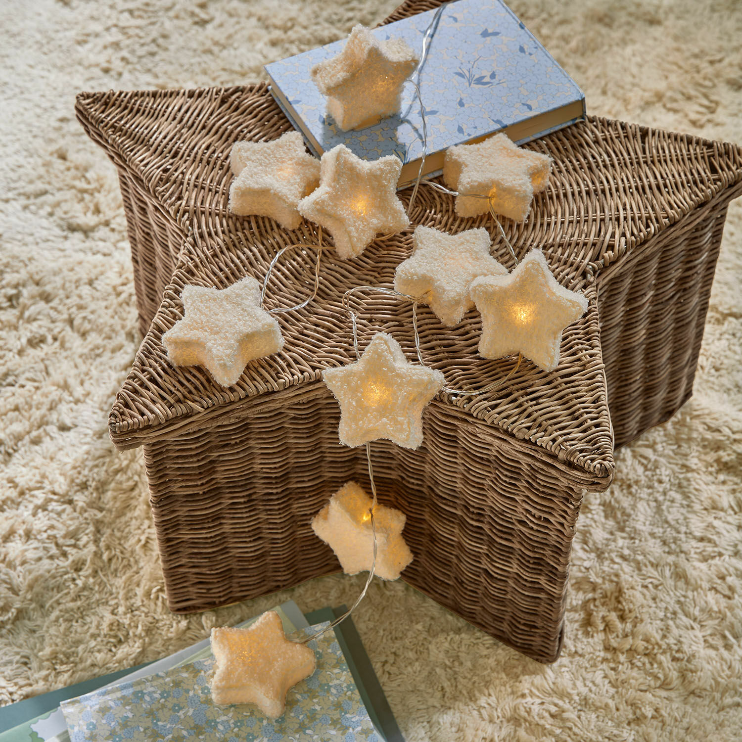Lichtsnoer Starwhisper Stervormige lichtslinger van zacht materiaal met warm licht op een rieten mand en tapijt, interieurdecoratie