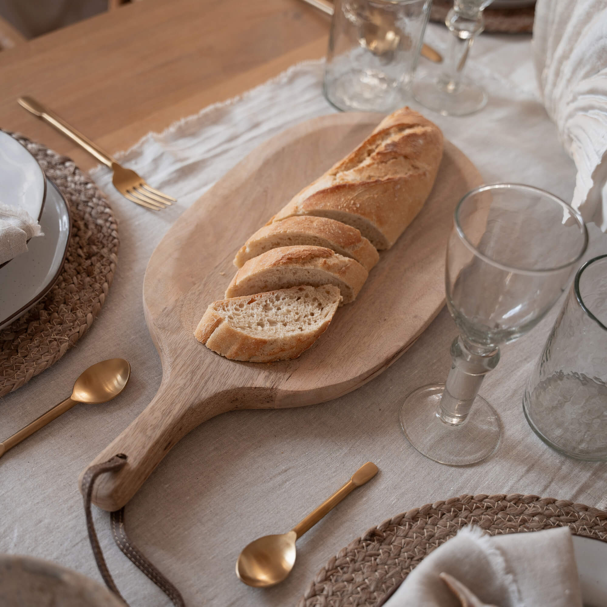 Houten snijplank met gesneden stokbrood op tafel met servies en gouden bestek