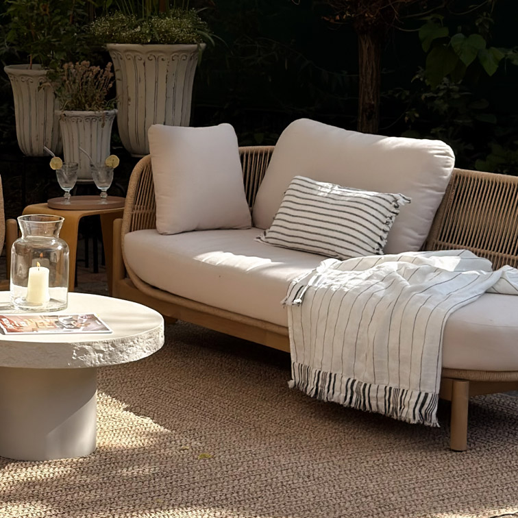 Moderne loungesofa met lichte kussens en gestreept plaid op natuurlijke buitenmat in tuin