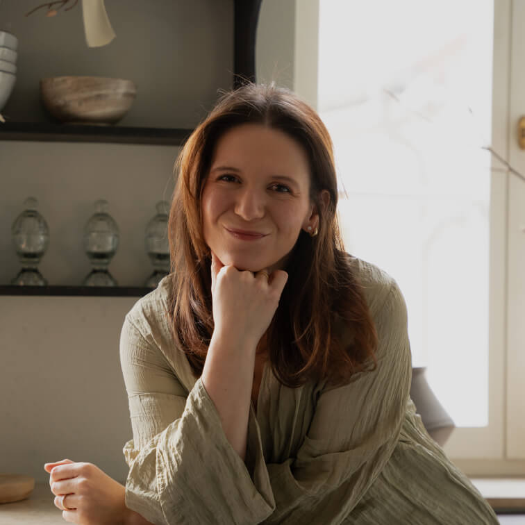 Lachende vrouw in groene linnen blouse zittend aan tafel in lichte kamer