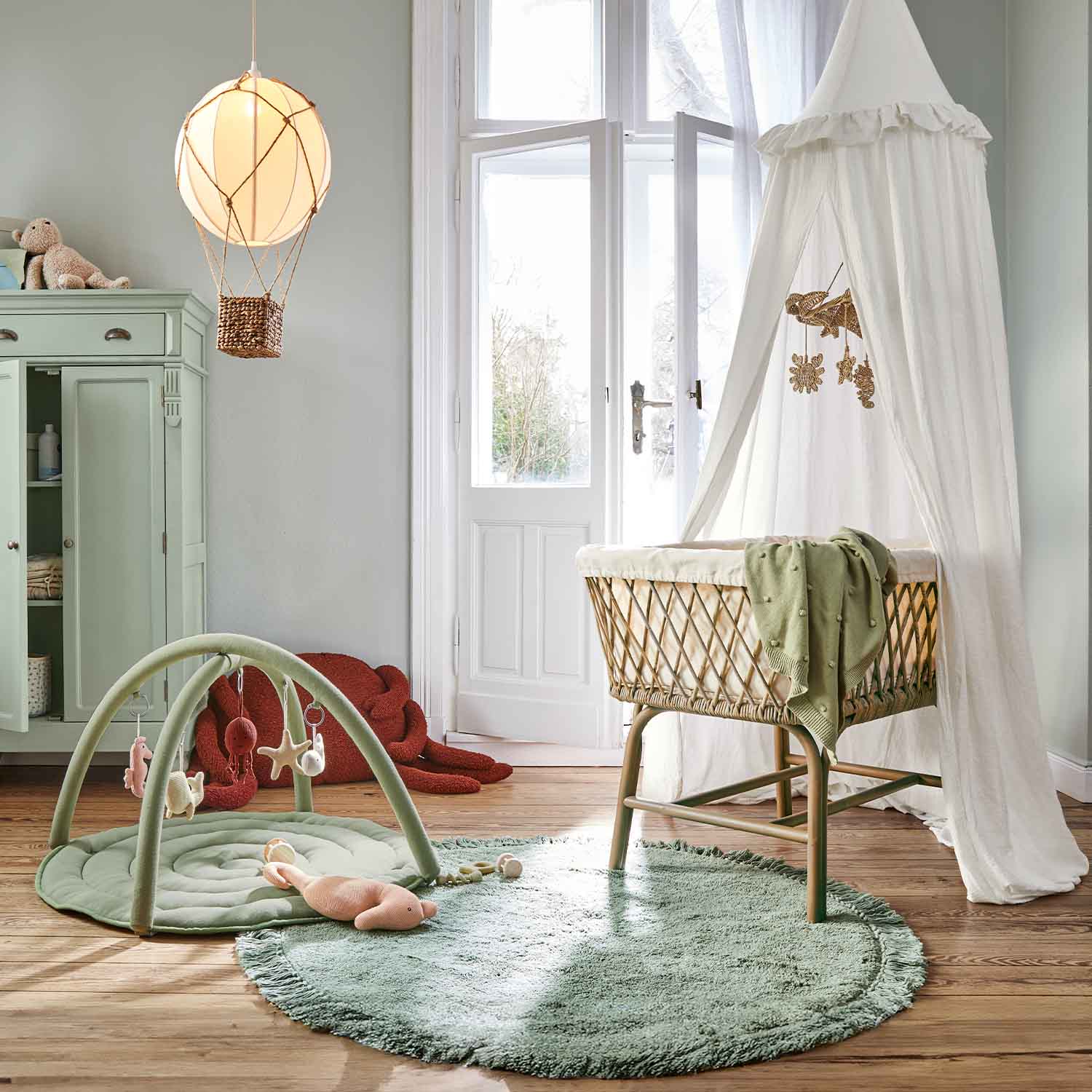 Kinderkamer met rotan wieg en witte hemel, groene vloerkleed en speelmat