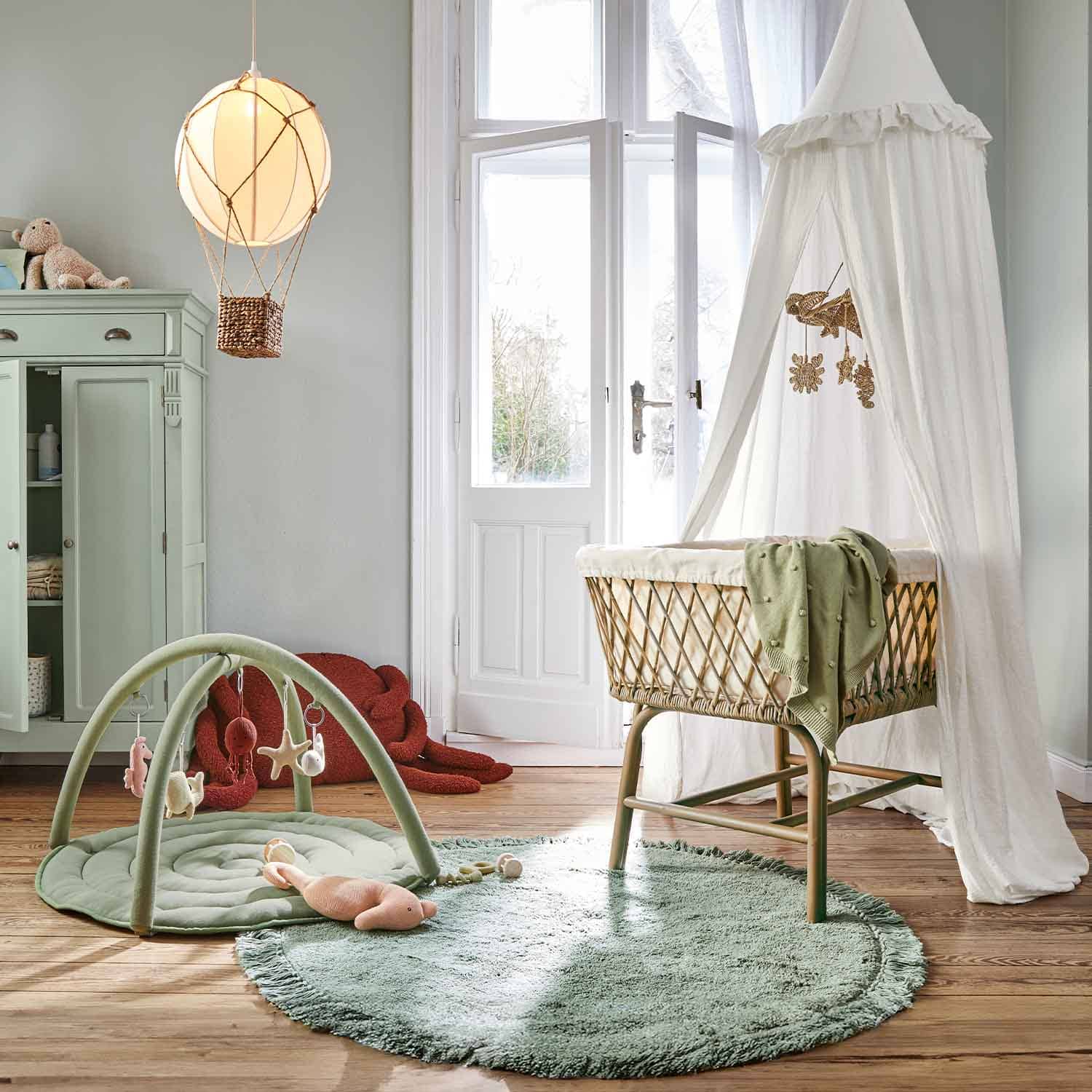 Kinderkamer met rotan wieg en witte hemel, groene vloerkleed en speelmat