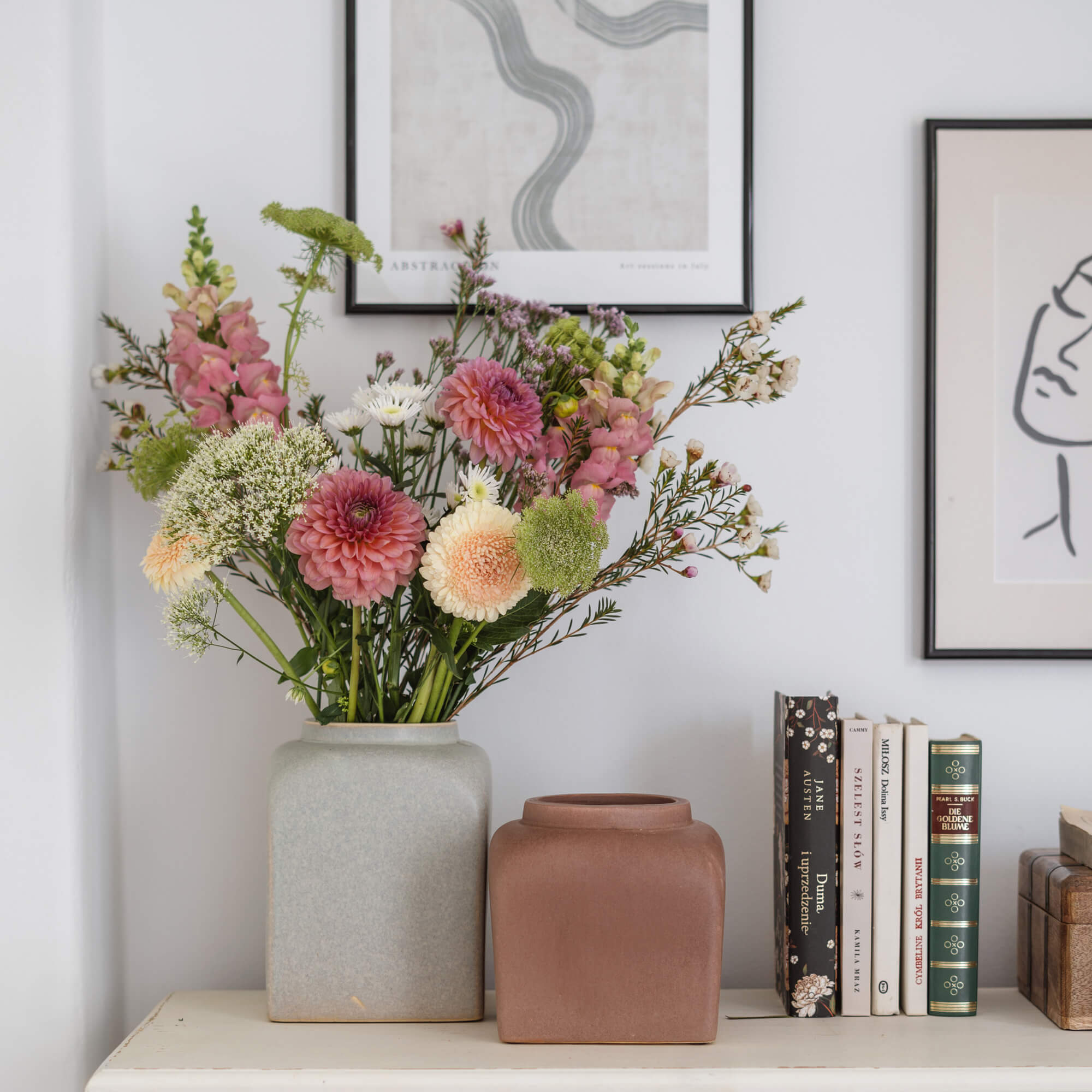 Twee keramische vazen in grijs en bruin op een witte tafel met bloemenboeket en boeken