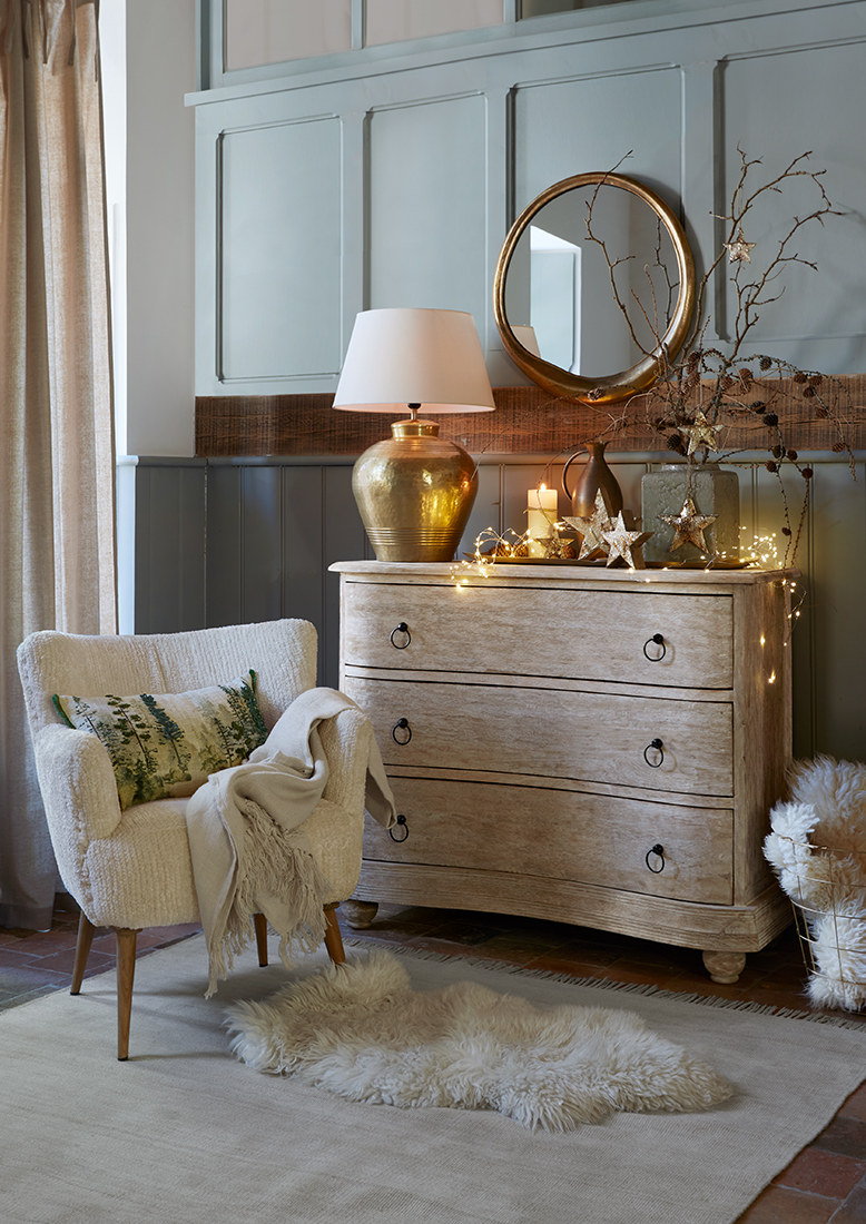 Lichte houten ladekast met kerstdecoratie en gouden lamp in gezellige woonkamer