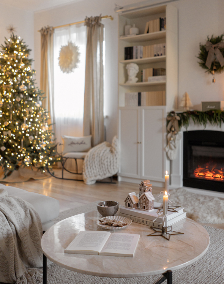 Gezellige woonkamer met lichte marmeren tafel, verlichte kerstboom en feestelijk versierde open haard