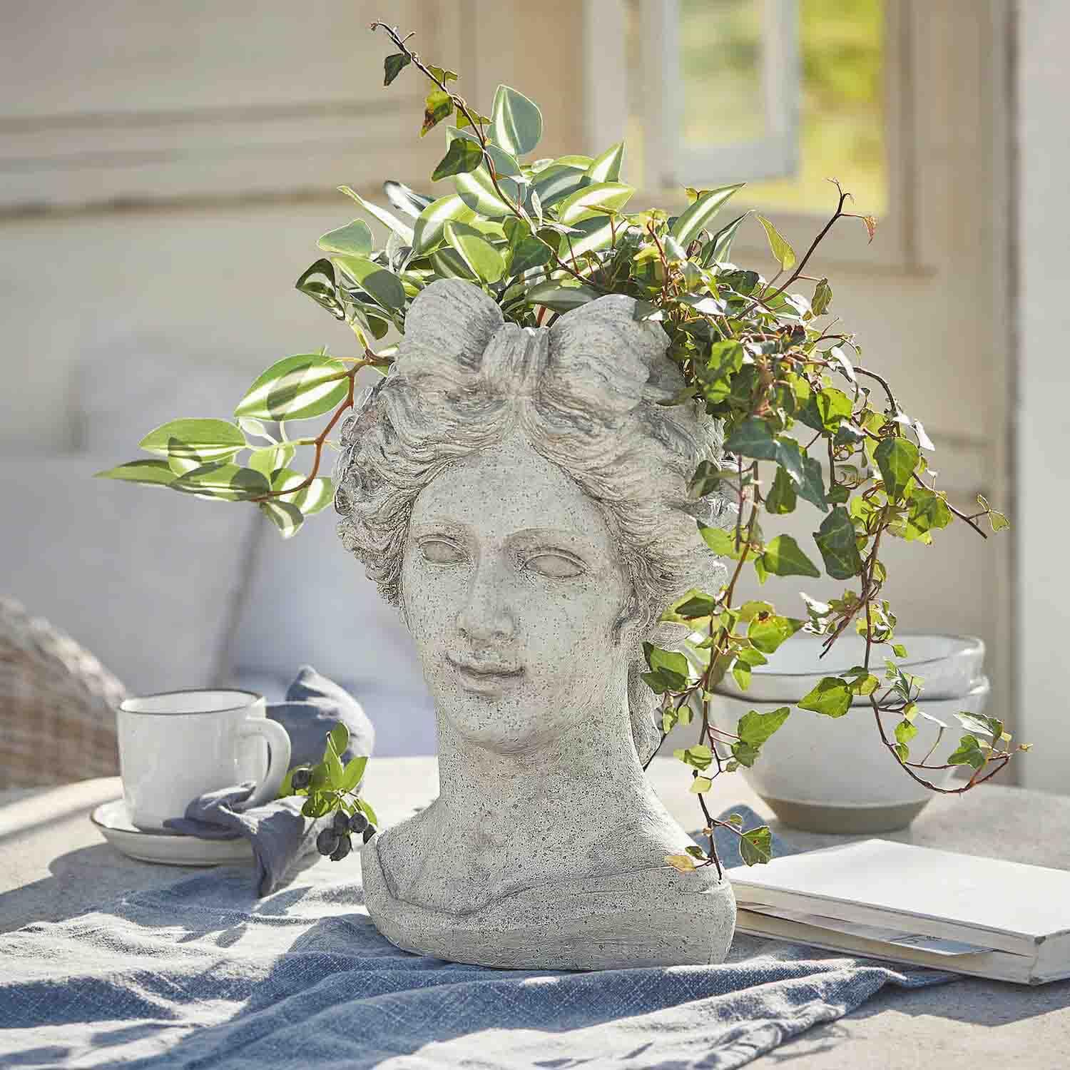 Bloempot in de vorm van een vrouwenhoofd van grijs steen met groene planten, tuindecoratie