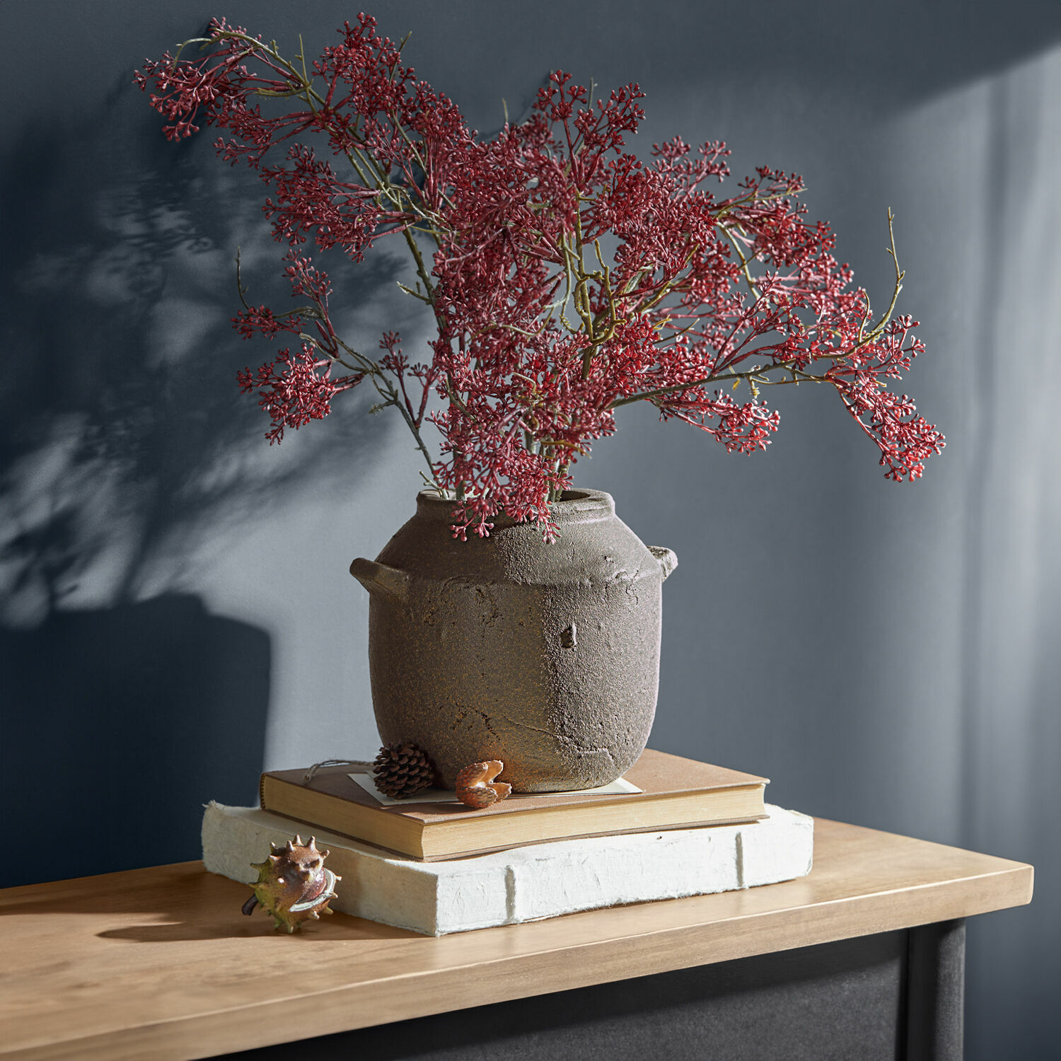 Rustieke bruine keramische vaas met rode takken op houten tafel met boeken