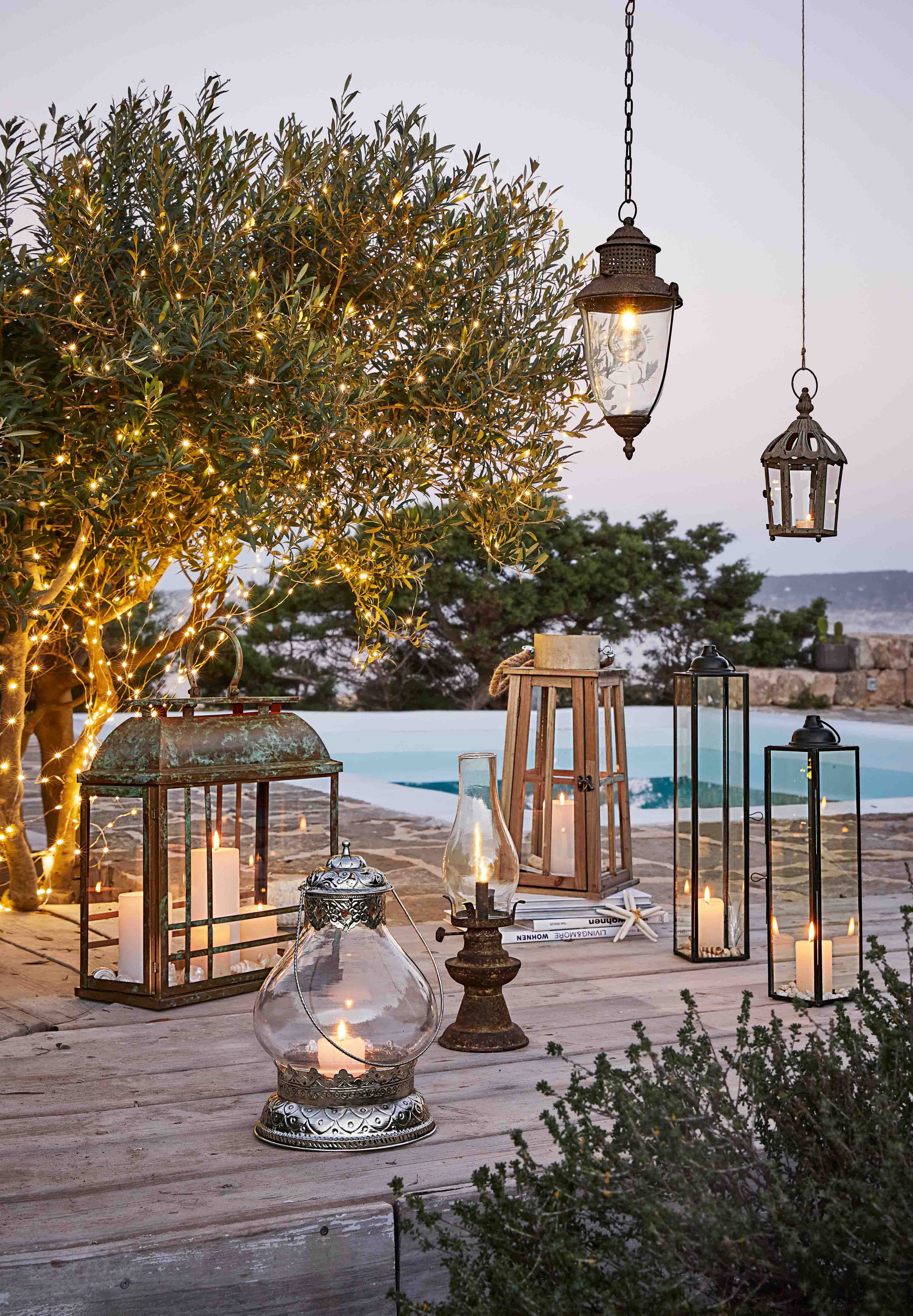 Set lantaarns en kaarsen op houten terras met boom versierd met LED-lichtjes