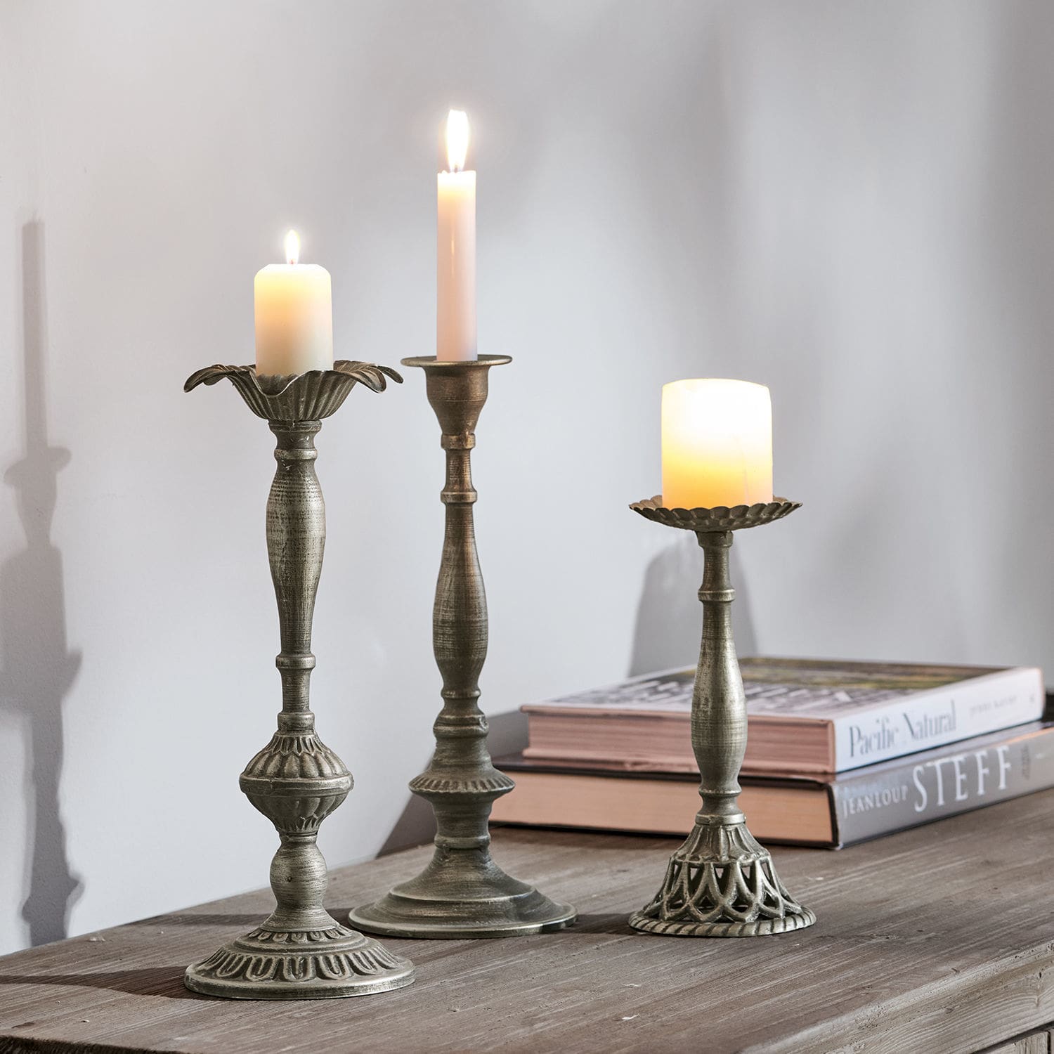 Kandelaar set van 3 Chandra Drie metalen kandelaren in antiek zilver met brandende kaarsen op een houten tafel