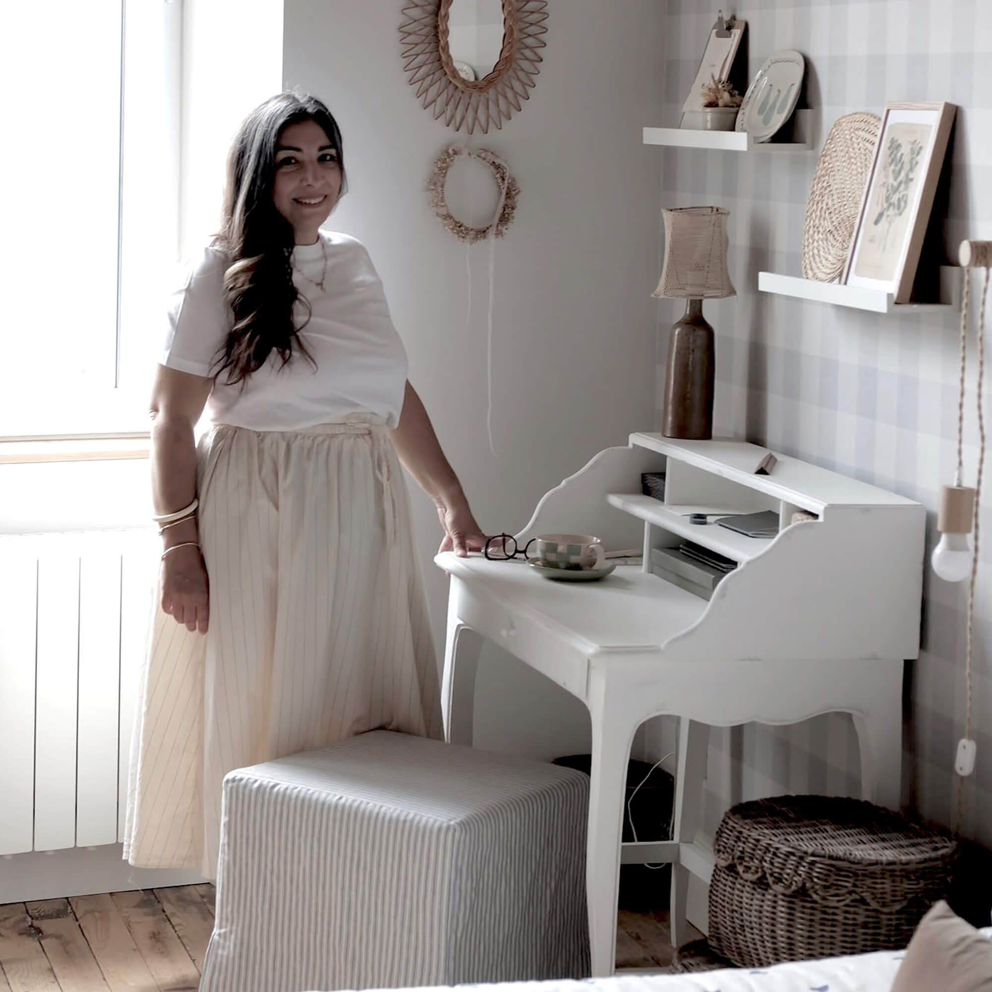 Vrouw in lichte rok naast wit houten bureau in gezellige kamer met natuurlijke decoraties