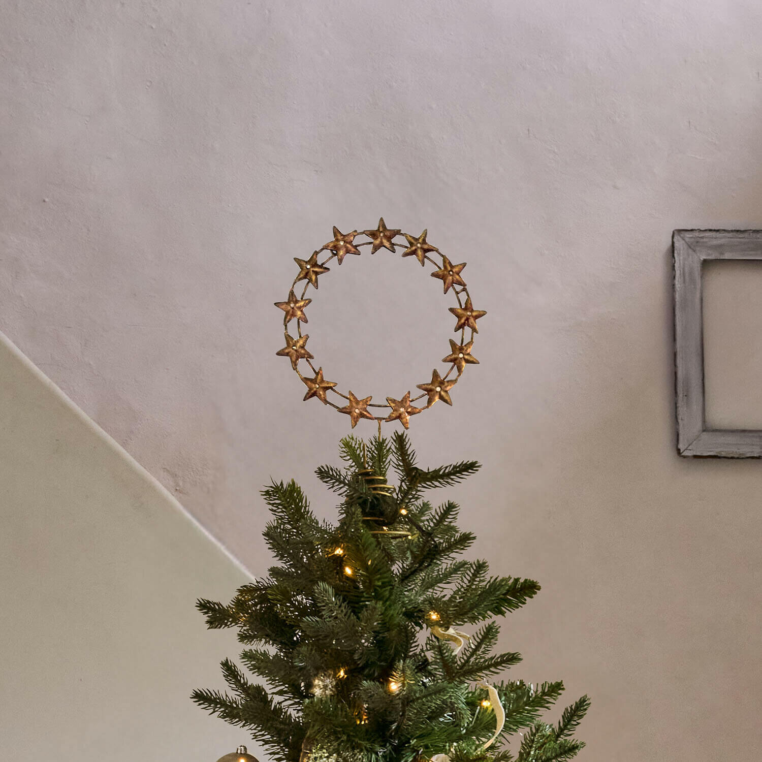 Kerstboompiek Tavelle Gouden sterkransdecoratie op de top van een groene kerstboom met sfeerverlichting