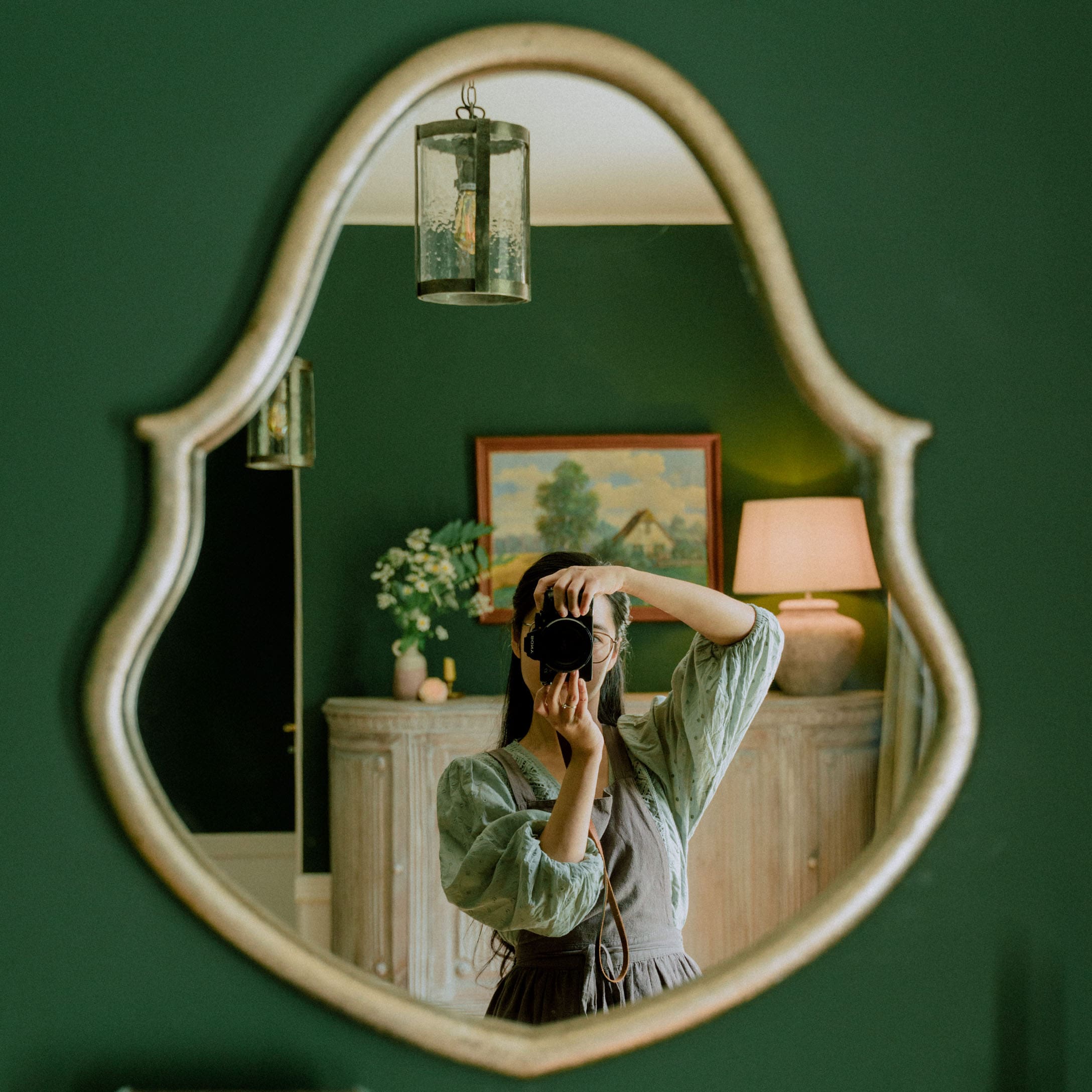 Ovaal spiegel met decoratieve lijst aan groene muur in stijlvolle kamer met lamp en schilderij