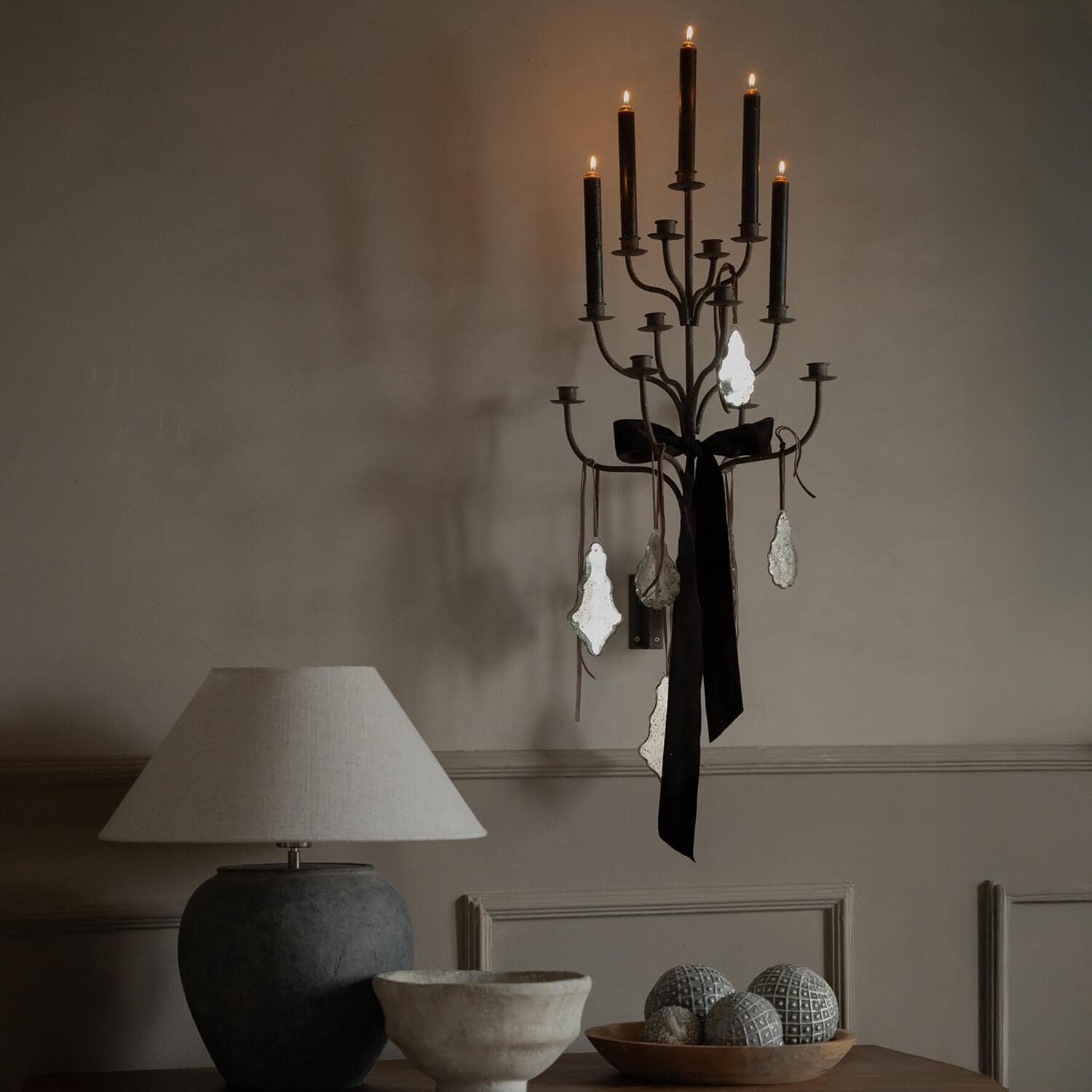 Metalen wandkandelaar met zwarte kaarsen en vintage decoraties tegen een beige muur in een gezellige ruimte