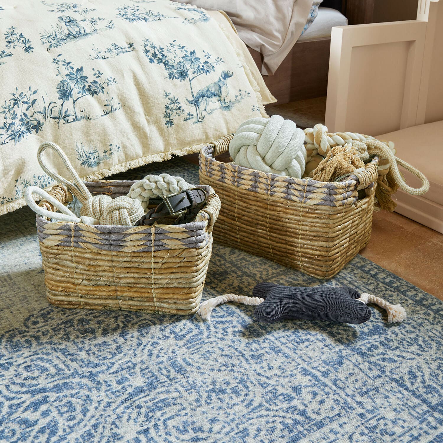 Twee natuurlijke rieten manden met hondenspeelgoed op een blauw tapijt in slaapkamer