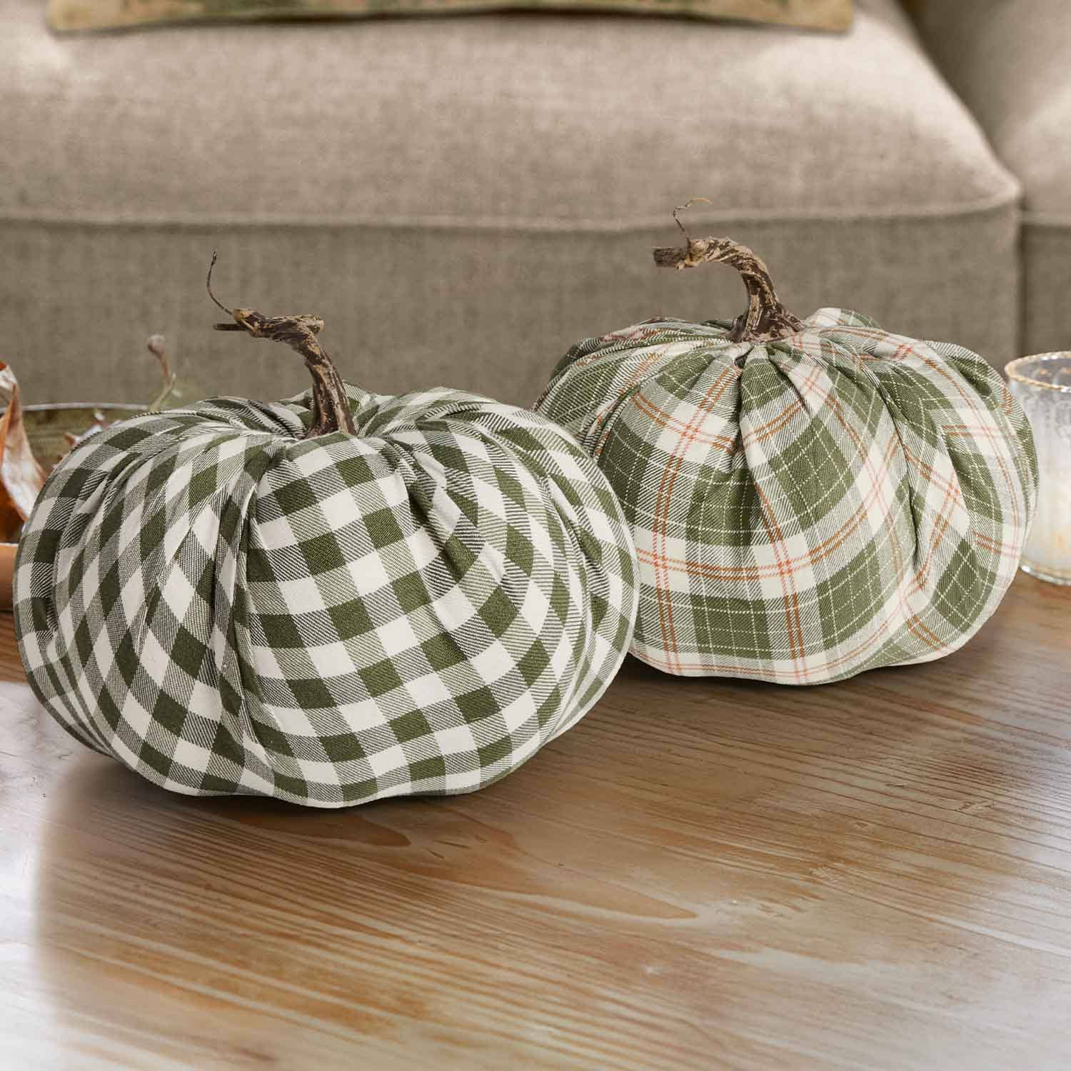 Twee decoratieve pompoenen van groen-wit geruit stof met natuurlijke stelen op een houten tafel