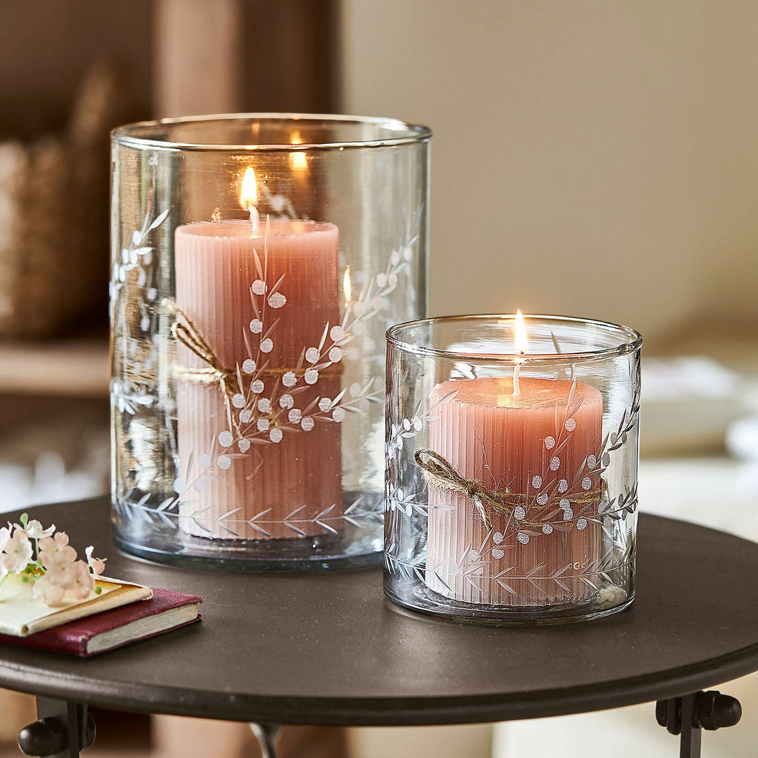 Windlicht set van 2 Temao Twee roze kaarsen in transparante glazen windlichten met wit plantenpatroon op een tafel