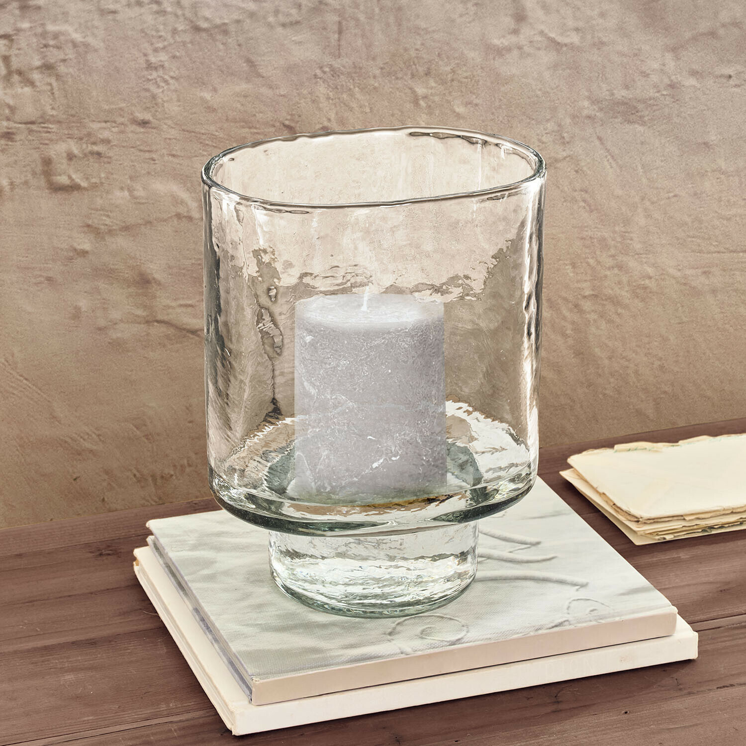 Transparante glazen windlicht met witte kaars op houten tafel naast boeken