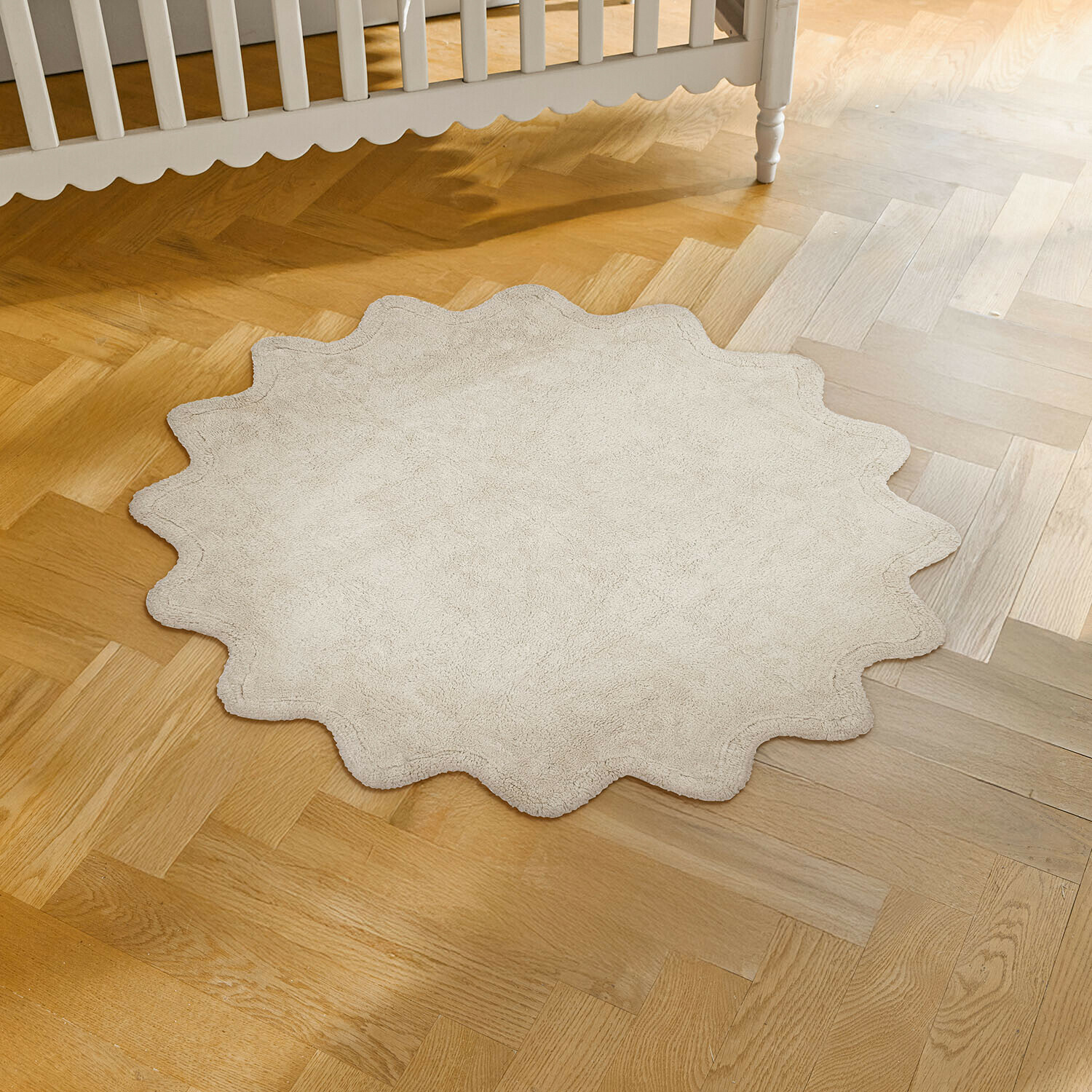 Ronde beige vloerkleed van zacht materiaal met golvende rand op lichte houten vloer