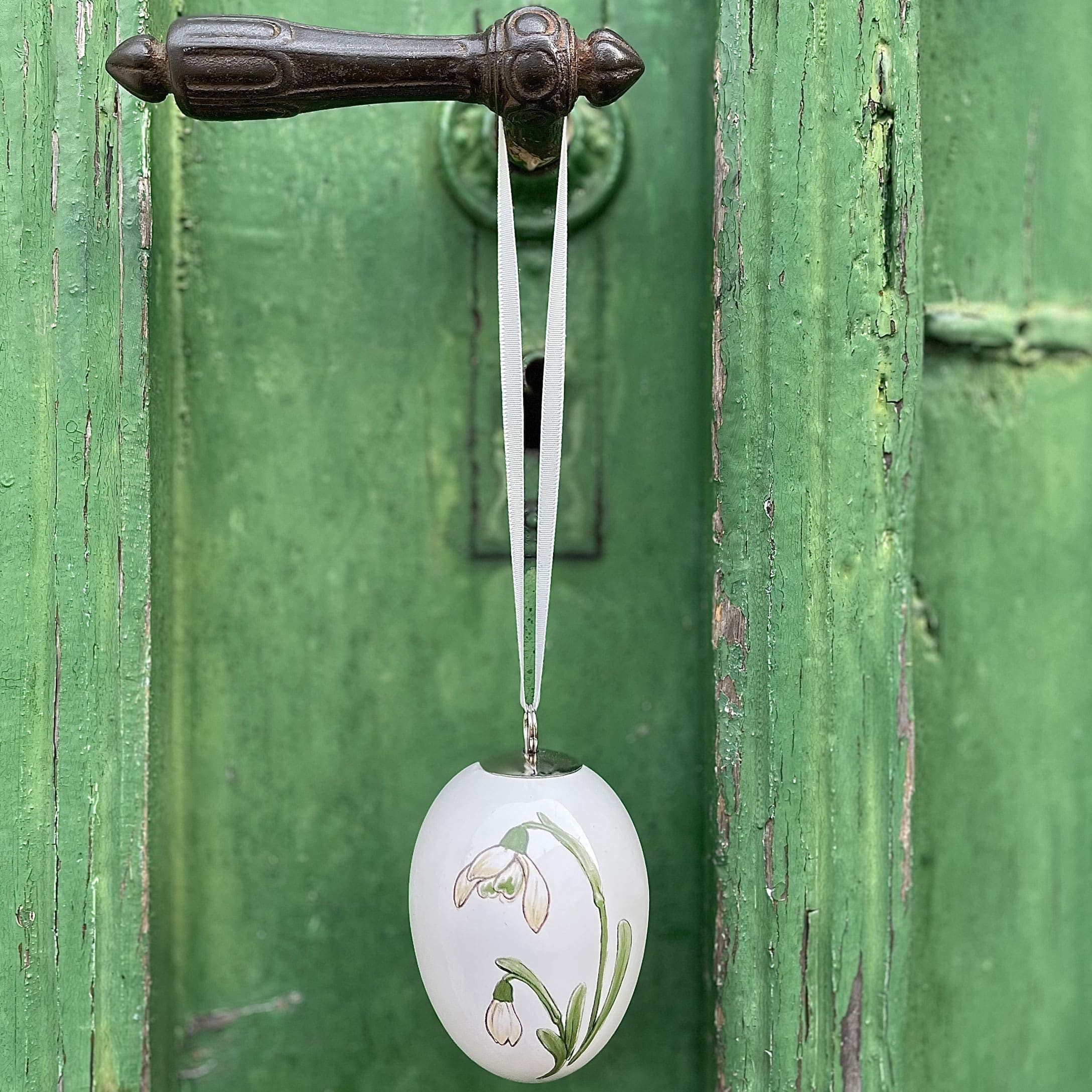 Witte keramische paasei-hanger met bloemmotief aan groene deur, lente decoratie