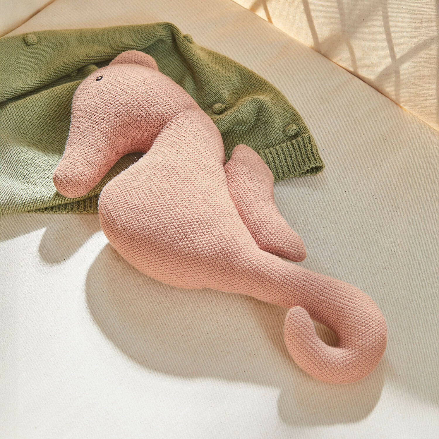 Knuffeltje Bubbilo Roze gebreide pluche zeepaardje op lichte achtergrond met groene trui, zacht kinderspeelgoed