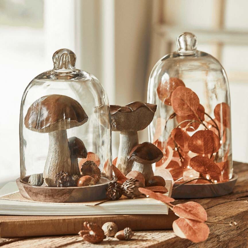 Decoratieve paddenstoelen en bladeren onder glazen stolpen op houten voet, herfsttafeldecoratie
