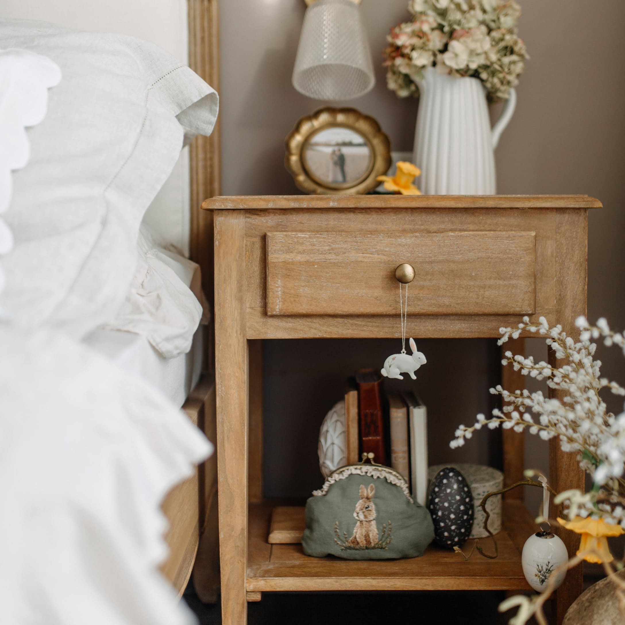 Houten nachtkastje met paasdecoraties en groene make-uptas met konijnenmotief in slaapkamer