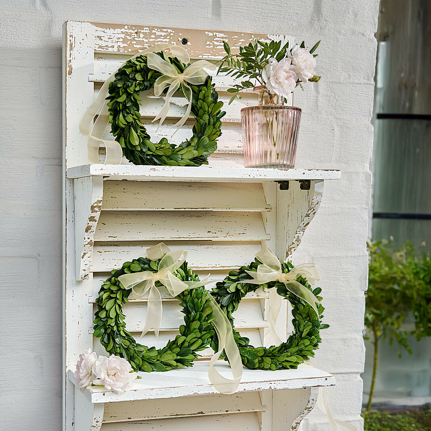 Decoratieve groene kransen van bladeren met crèmekleurige strikken op witte vintage houten plank