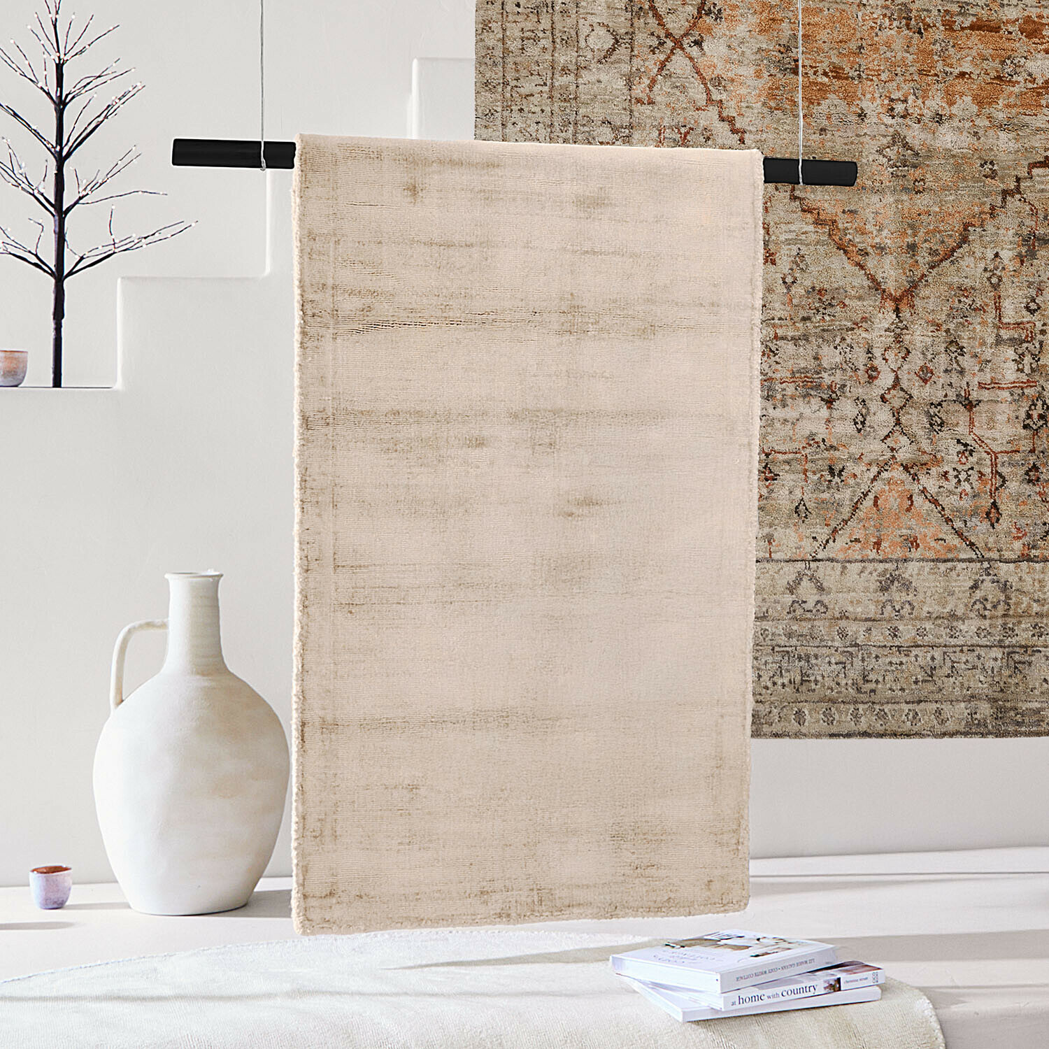 Beige vloerkleed van zacht materiaal aan zwarte stang in lichte ruimte met decoraties