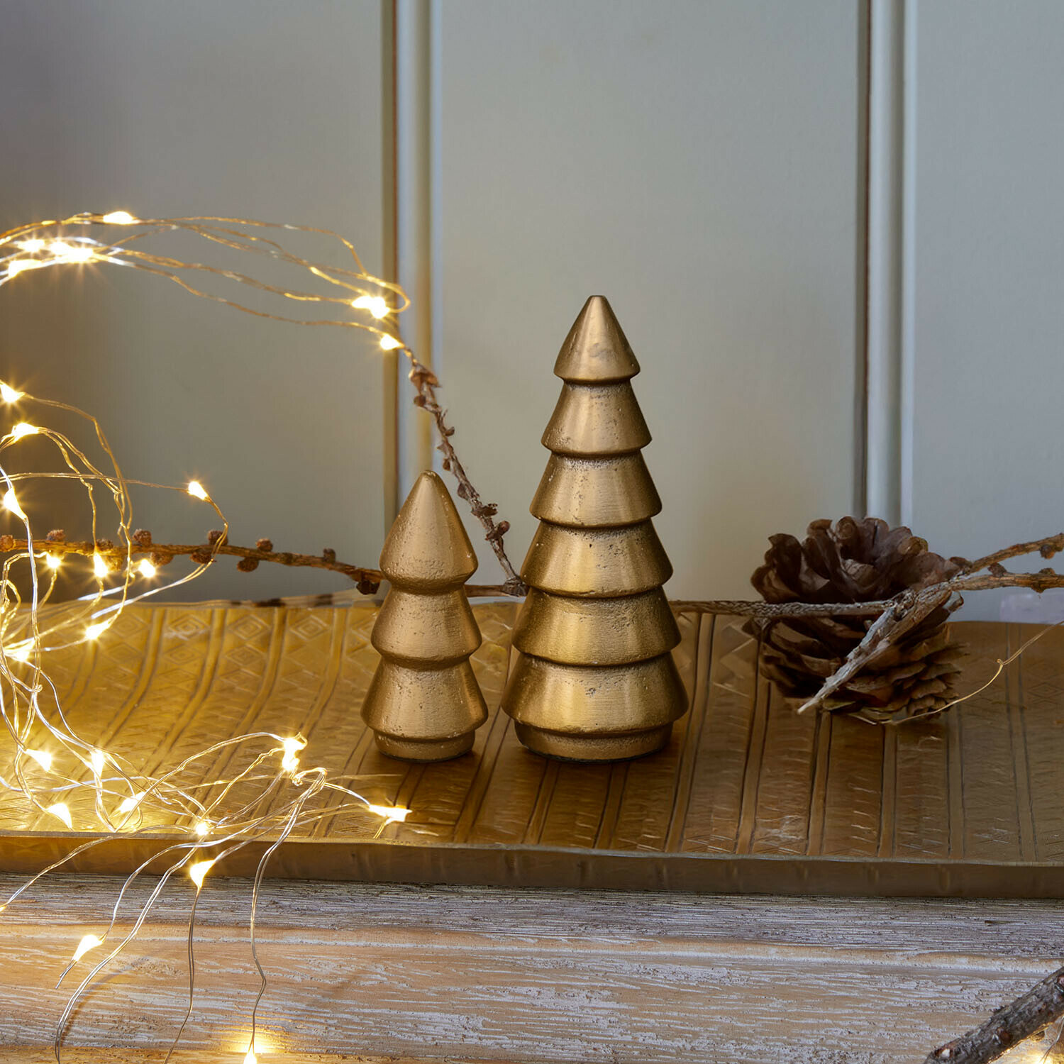 Decoratieve boom set van 2 Zarilith Gouden metalen kerstboomdecoraties op gouden schaal met LED-lichtjes en dennenappel op houten tafel