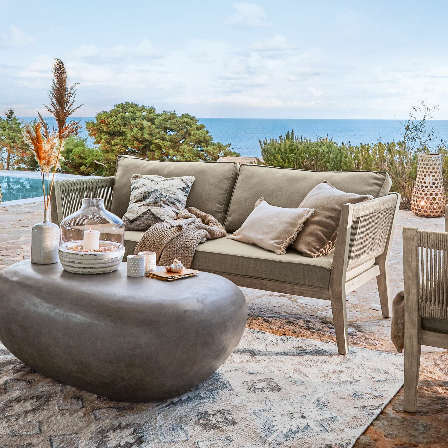Bank Biarritz Beige buitenbank van hout en stof op terras met zeezicht, moderne stenen salontafel