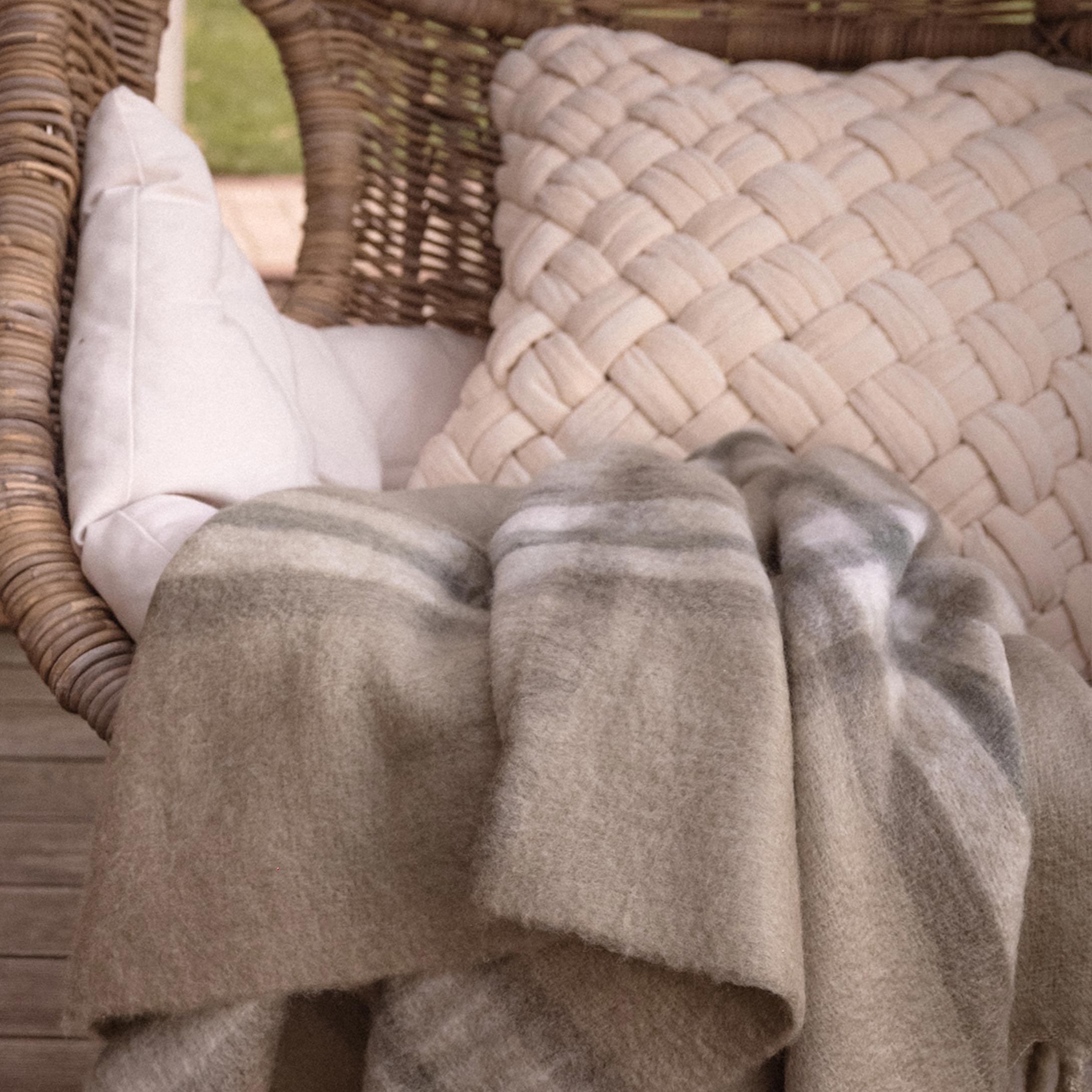 Beige zachte deken met strepen op rotan stoel met kussens op terras