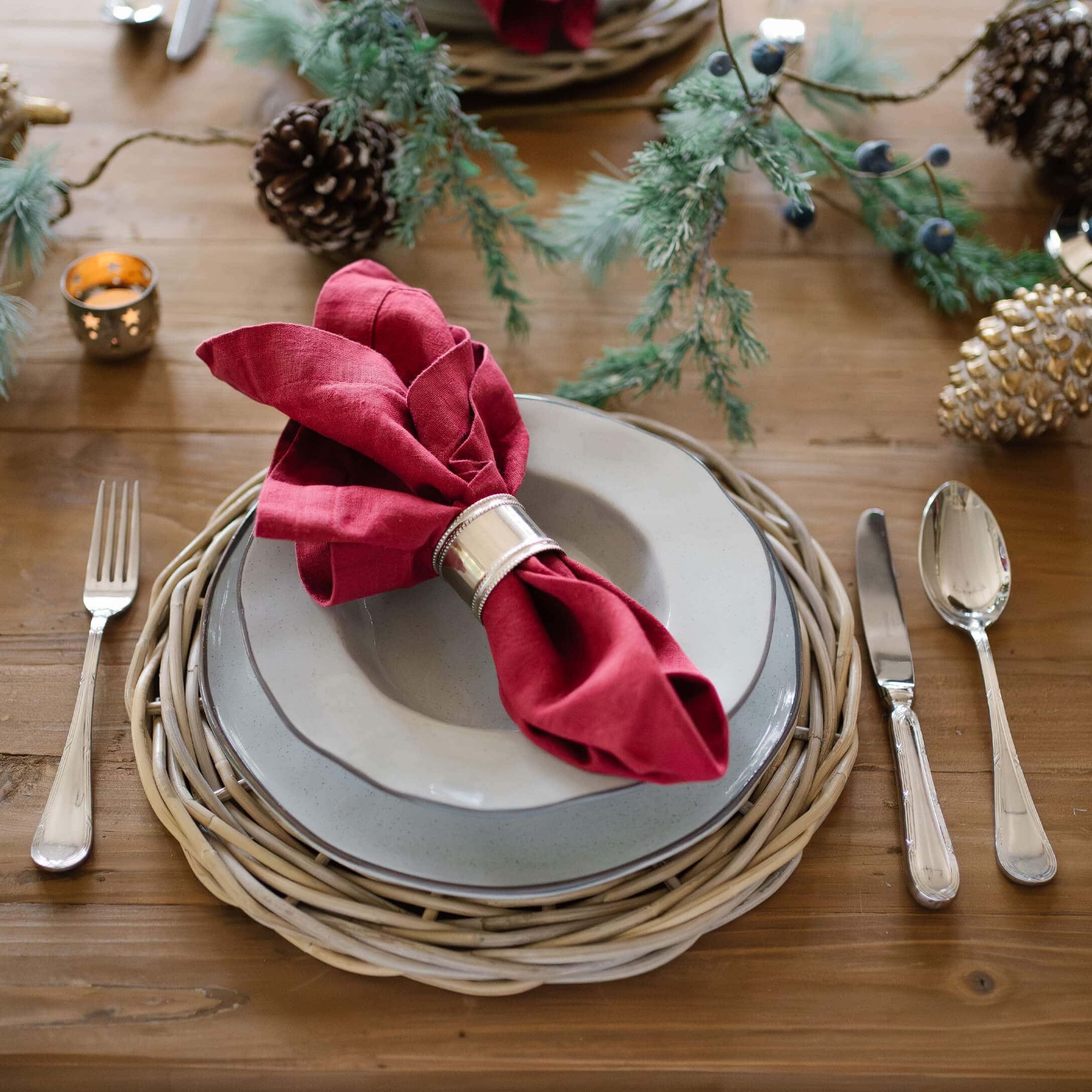 Elegante tafelsetting met grijze borden, rode linnen servetring en natuurlijke rieten onderzetter