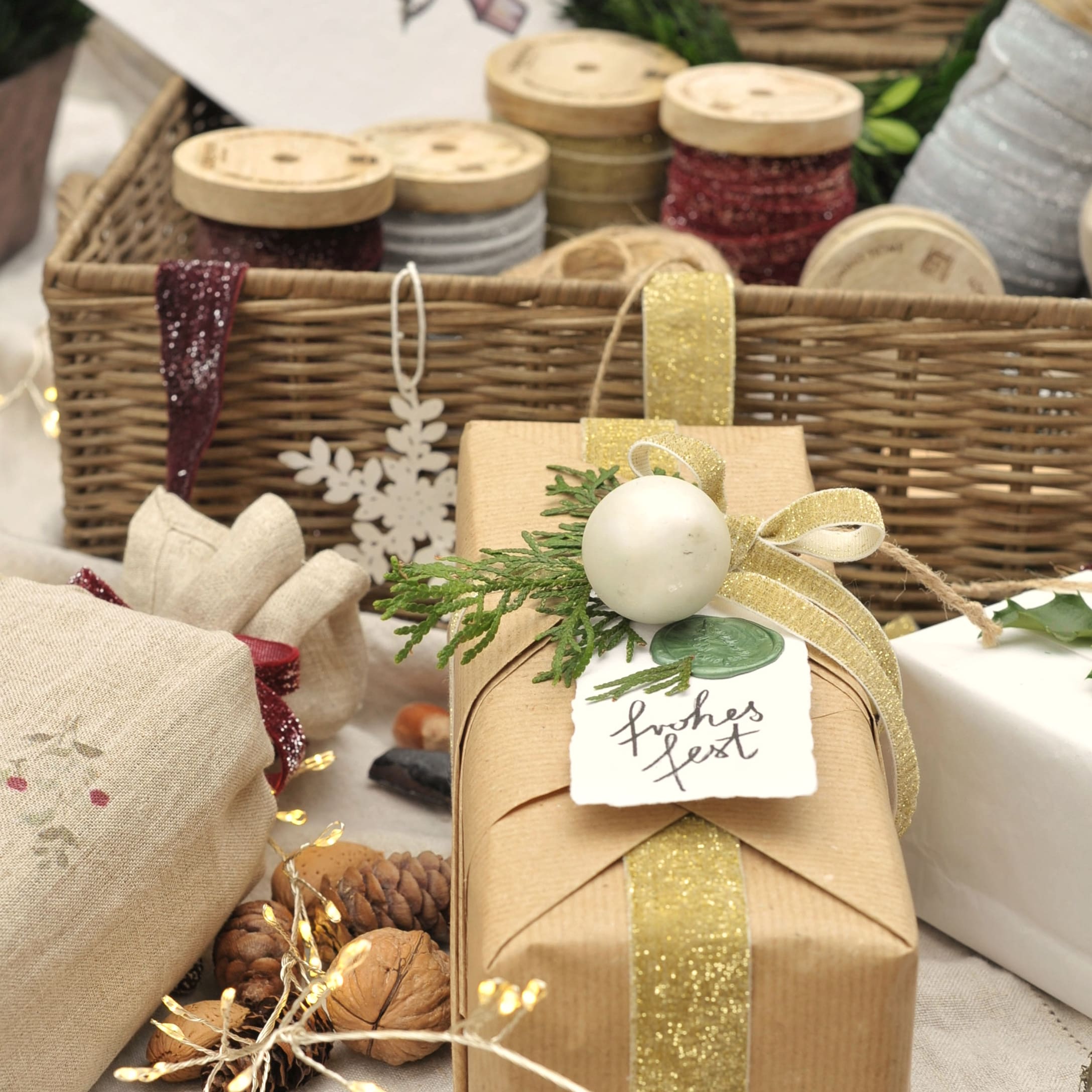 Cadeau verpakt in bruin papier met gouden lint en groene decoratie, lintrollen op de achtergrond