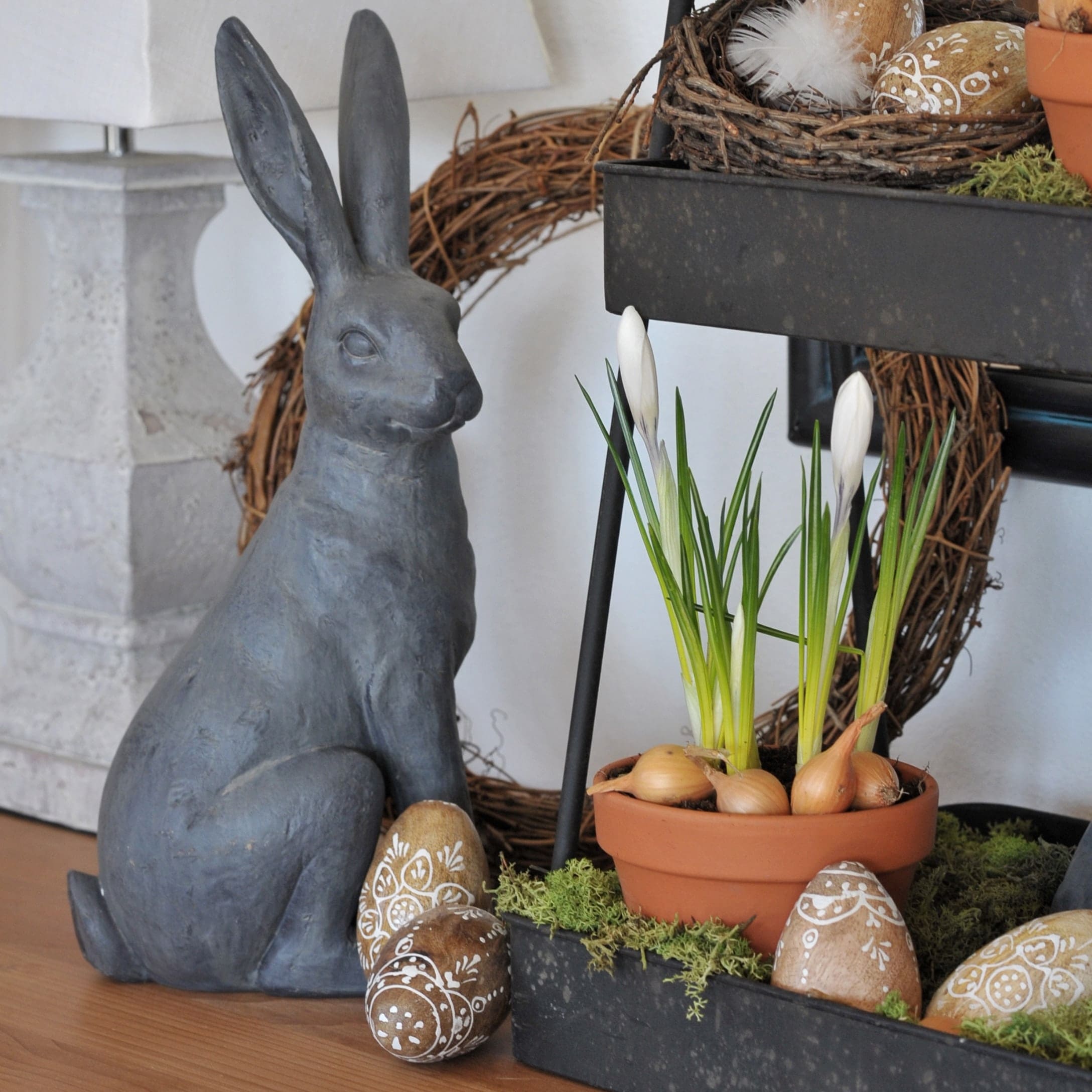 Grijze keramische haas naast pot met witte bloemen en versierde paaseieren voor lenteversiering