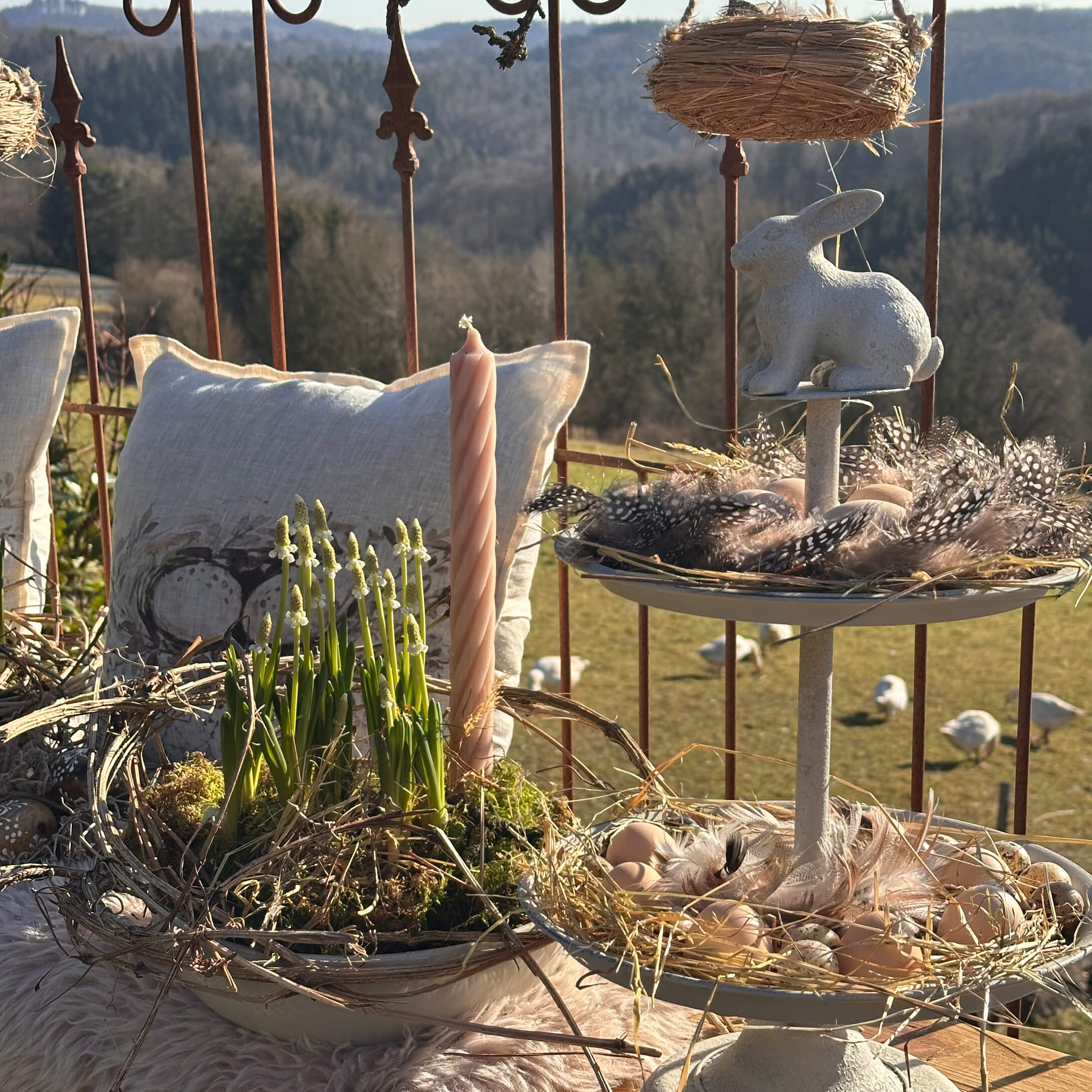 Natuurlijke paasdecoratie met witte haas, veren en kaars op rustieke achtergrond met kussens