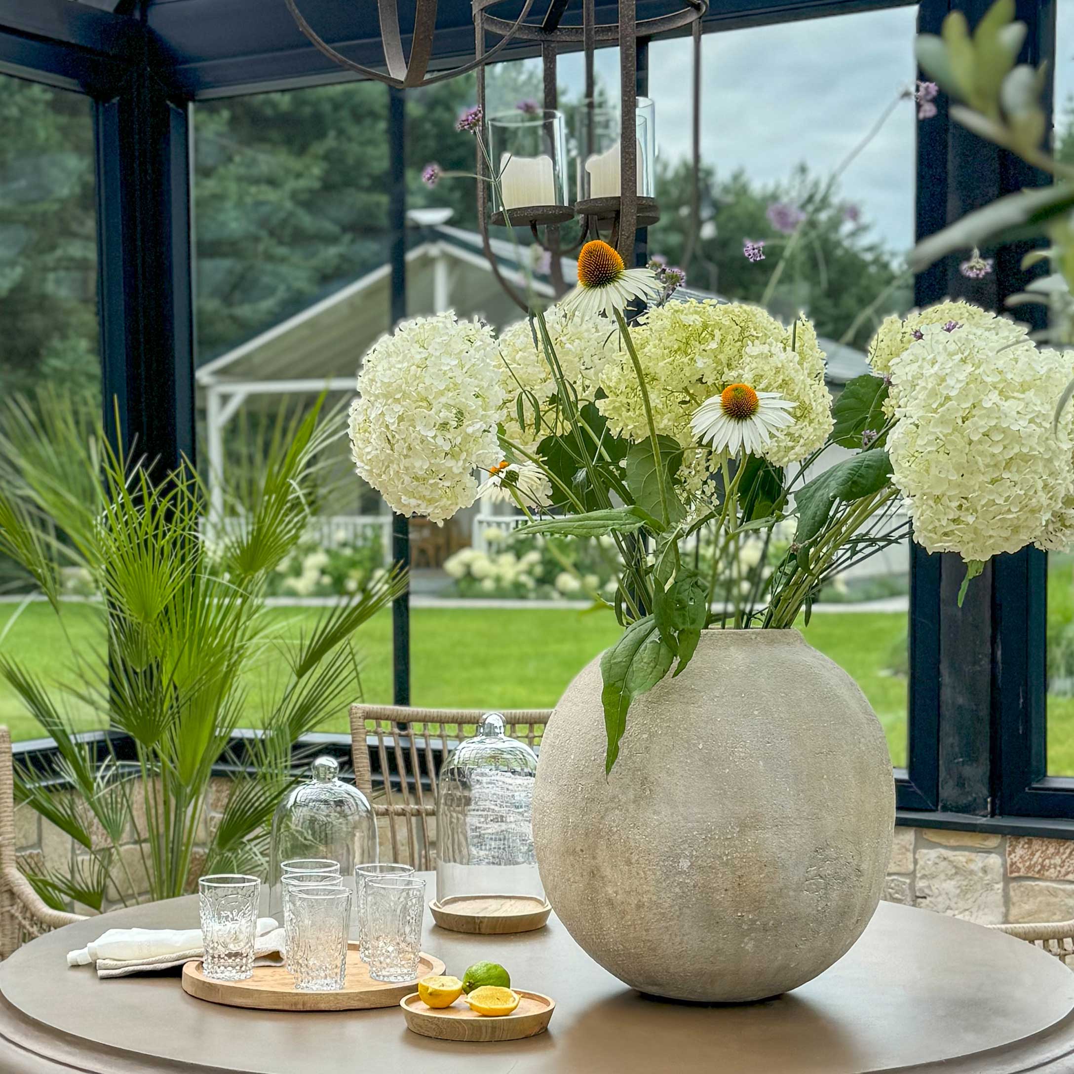 Grote ronde betonnen vaas met witte bloemen op tuintafel met decoratieve glazen