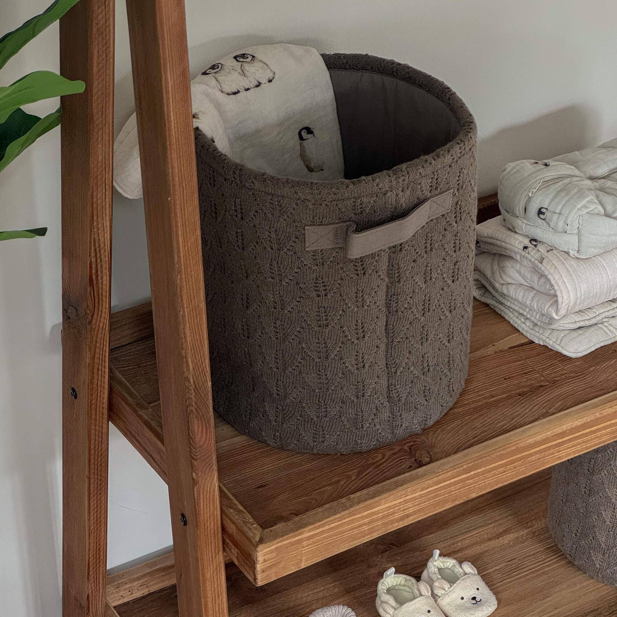 Bruine gebreide opbergmand op houten plank met zachte stof en beige babyslofjes