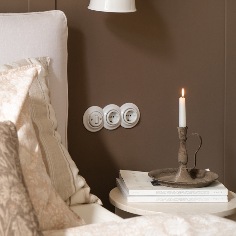 Rustieke metalen kandelaar met witte kaars op tafeltje naast bed met beige beddengoed