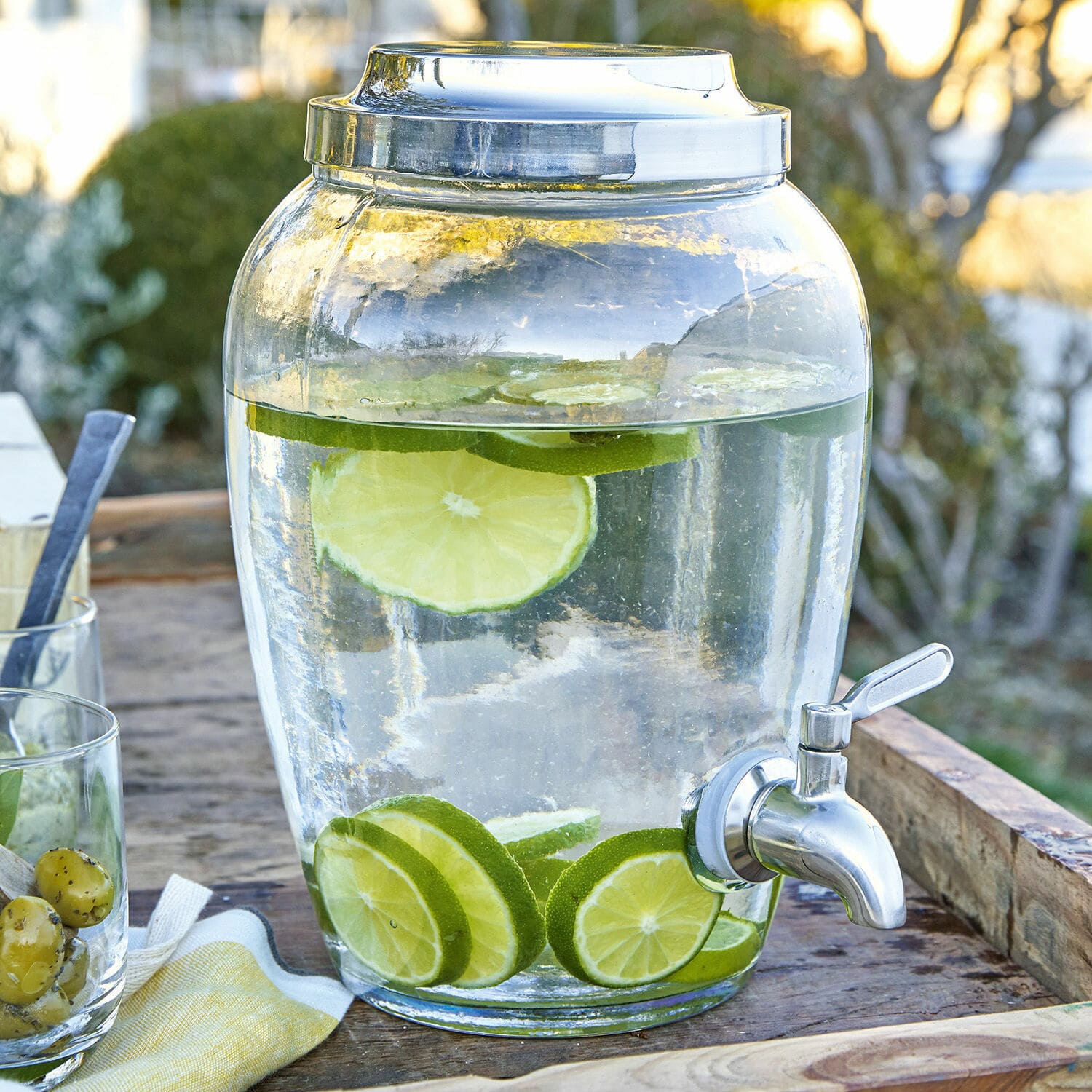 Glazen drankdispenser met kraan, water met limoenplakjes op houten tafel