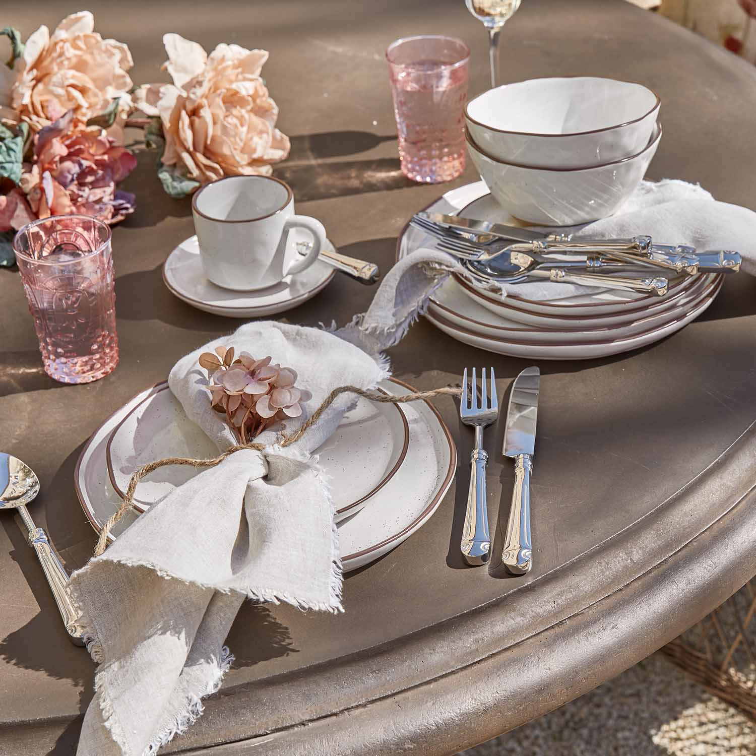 Witte keramische servies met bruine rand, roze glazen en bestek op tafel