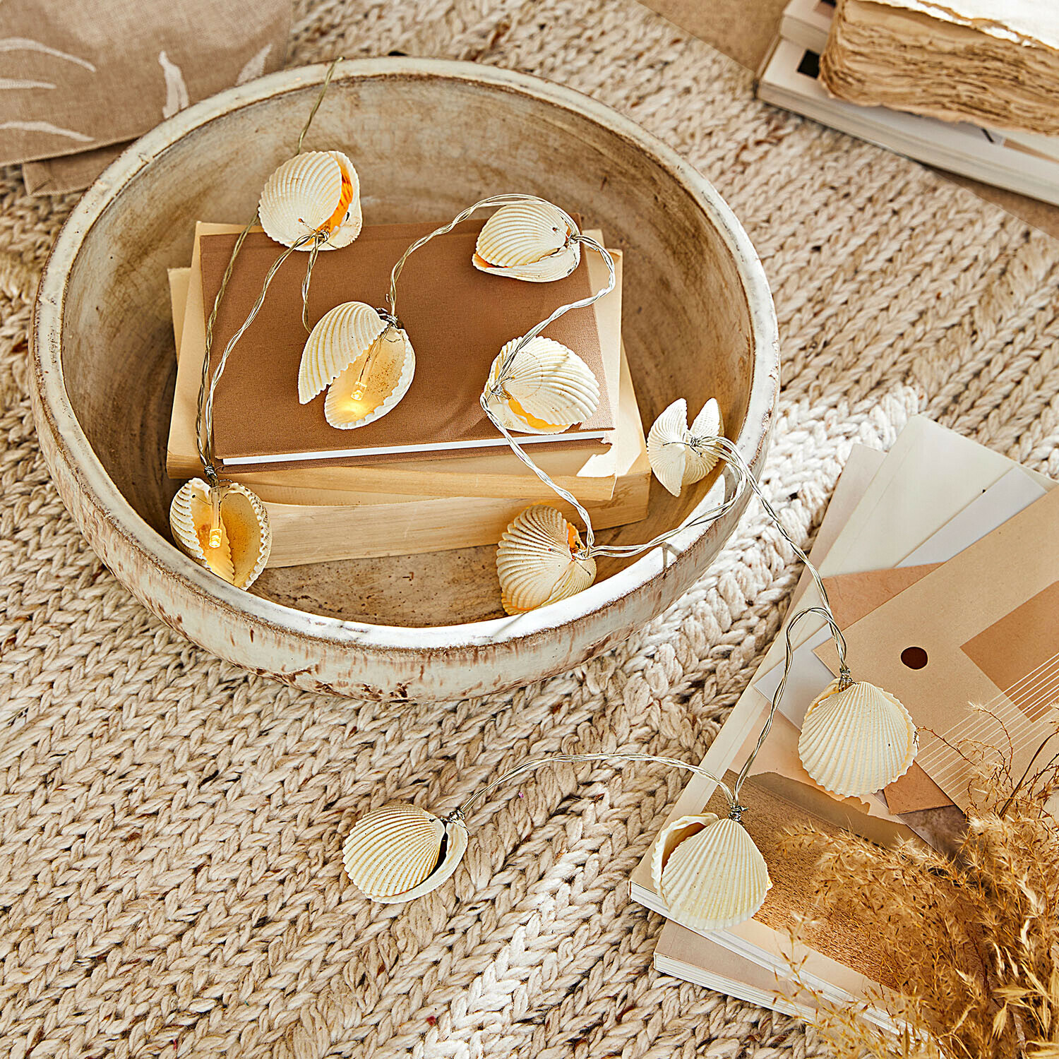 Sfeerverlichting met natuurlijke schelpen op beige achtergrond met houten schaal en boeken