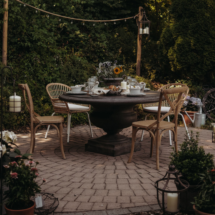 Ronde donkere houten tuintafel met rotan stoelen op een betegeld terras met kaarsen en bloemen versierd