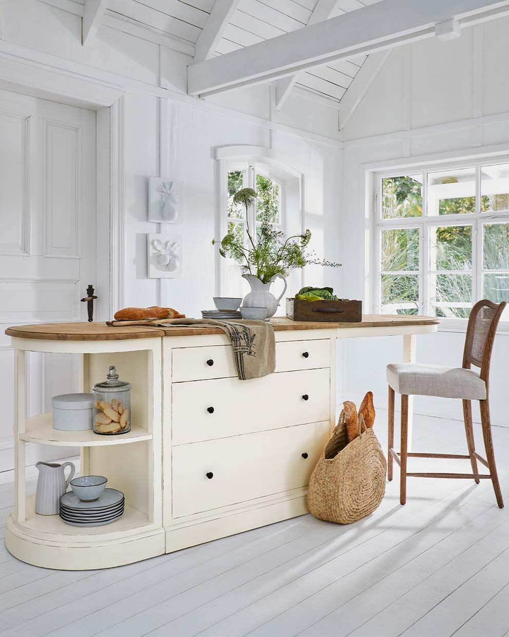 Crèmekleurig keukeneiland met houten blad en lades, versierd met vaas met bloemen en broodmand