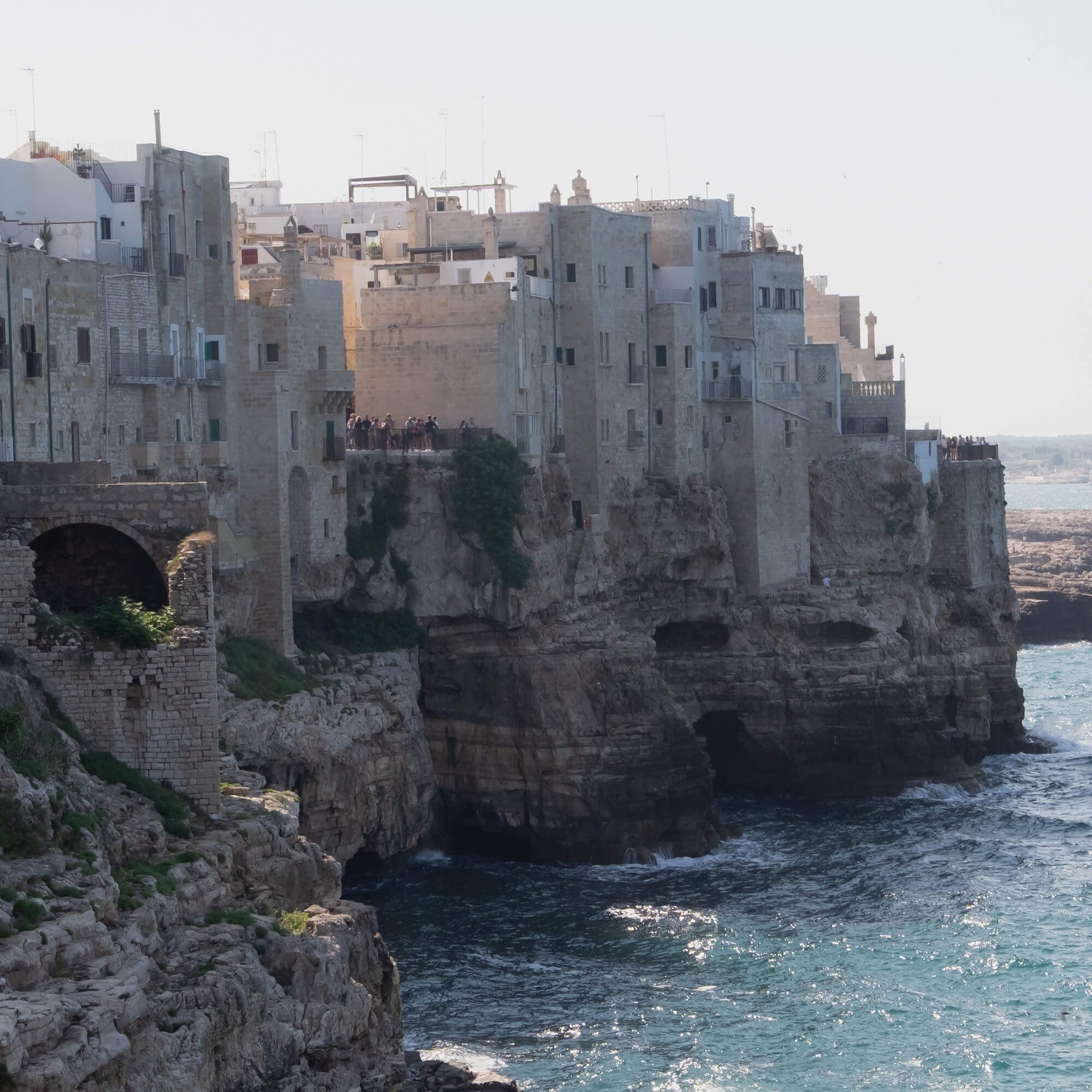 Oude stenen gebouwen op een klif boven de zee met turquoise water en rotsen eronder