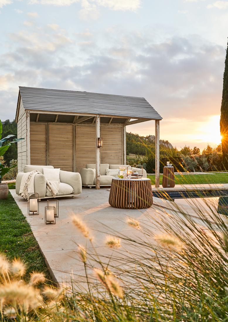 Gezellig wit tuinpaviljoen met beige meubels en houten tafel op terras bij zonsondergang