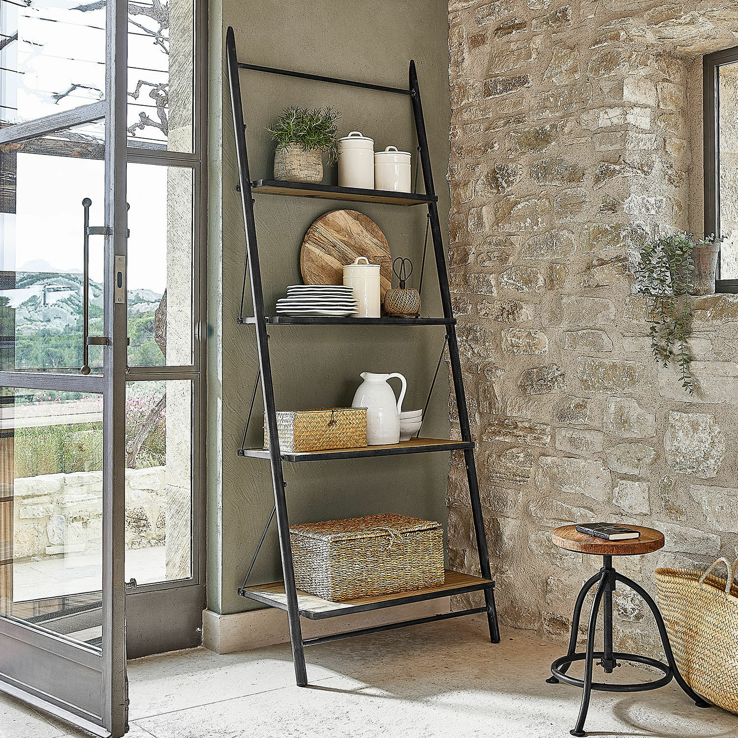 Ladderrek Greenbriar Zwarte metalen ladder met houten planken en decoraties in rustieke ruimte met stenen muur