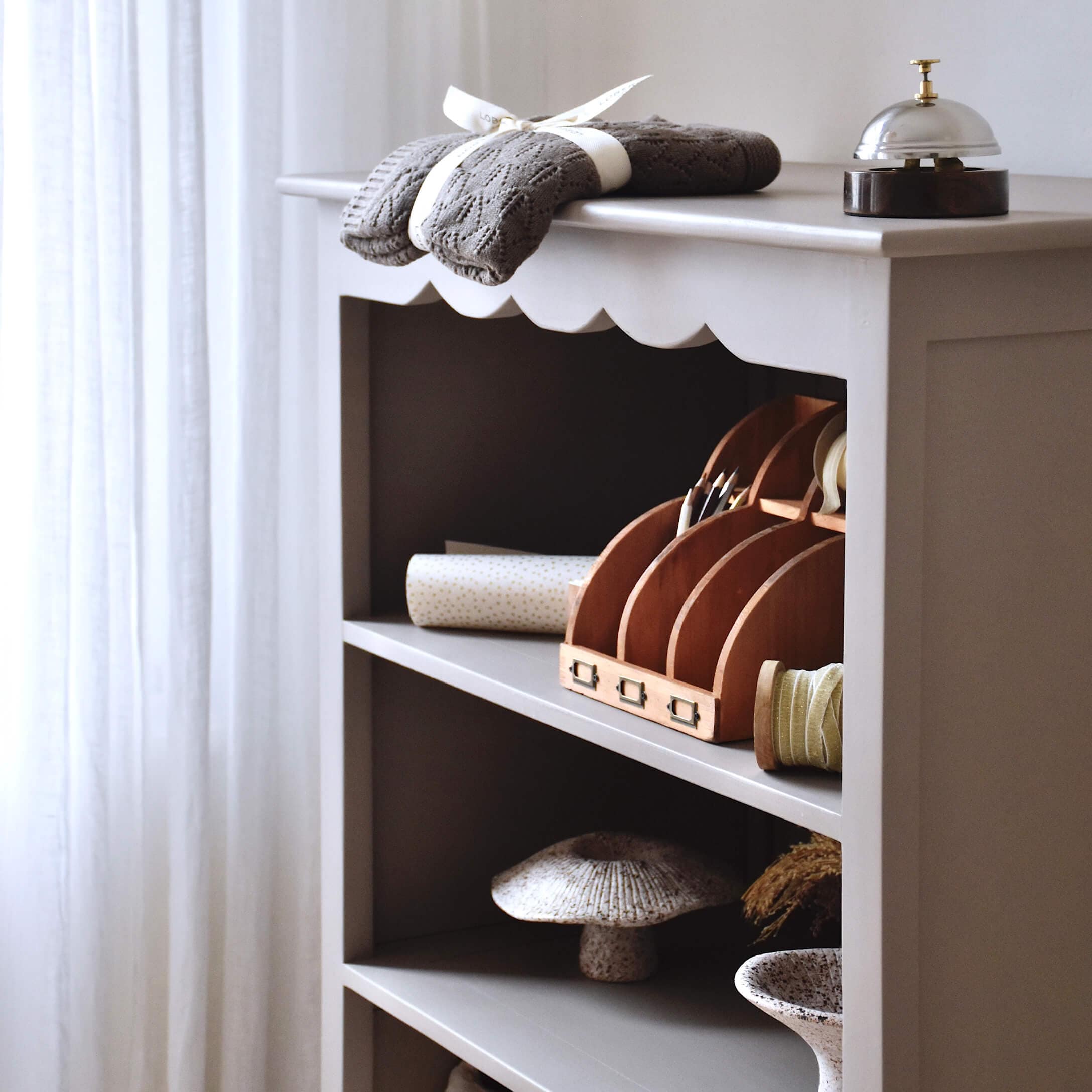 Grijze houten plank met decoratieve items en grijze gebreide stof erop